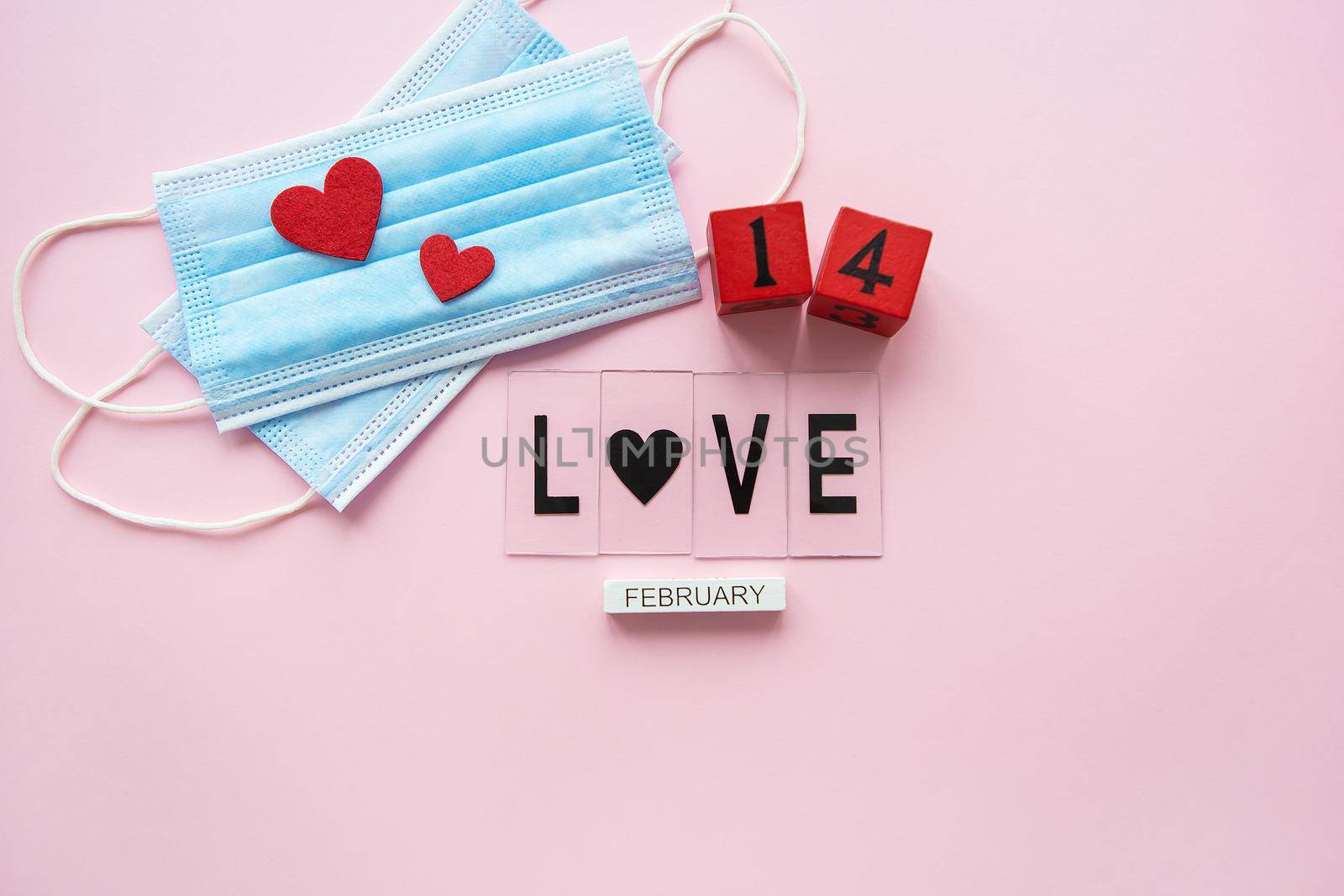 Valentine's Day celebration concept. Wooden cubes 14 February on a pink background. The heart lies on medical masks, the fight against coronavirus. by sfinks