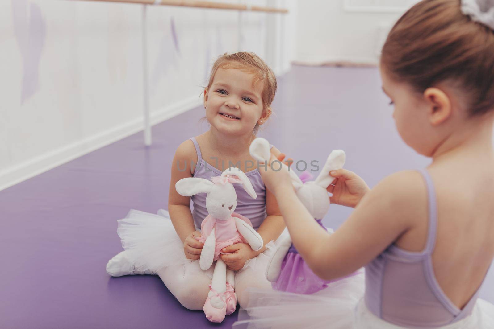 Happy little cute girl wearing tutu and leotard laughing joyfully, enjoying ballet lesson at dance school. Adorable little ballerinas resting after exercising and dancing, copy space