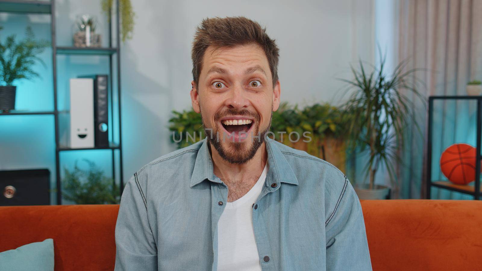 Oh my God, Wow. Handsome adult man surprised looking at camera with big eyes, shocked by sudden victory, good win news, celebrating at home. Excited amazed young guy indoors in living room on couch