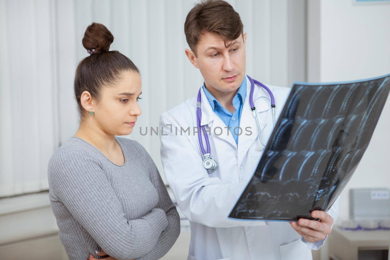 Mature male doctor examining MRI scan of his female patient during medical appointment