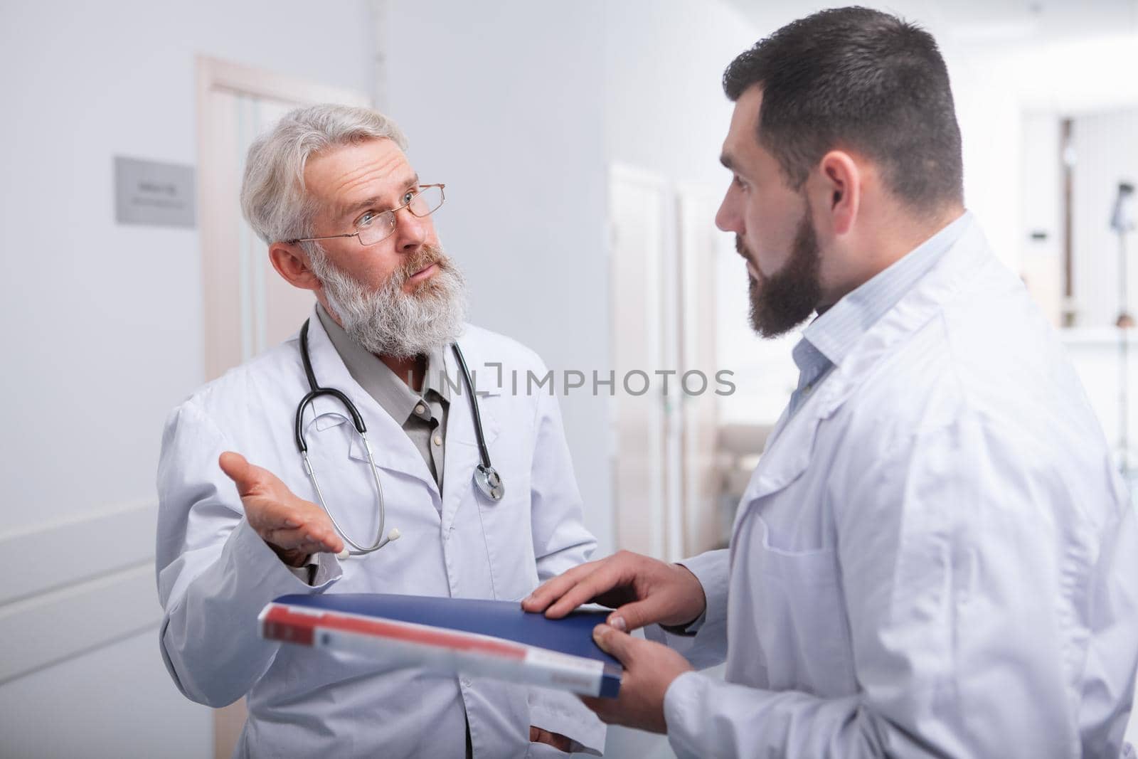 Senior male doctor talking to a colleague at the hospital by MAD_Production