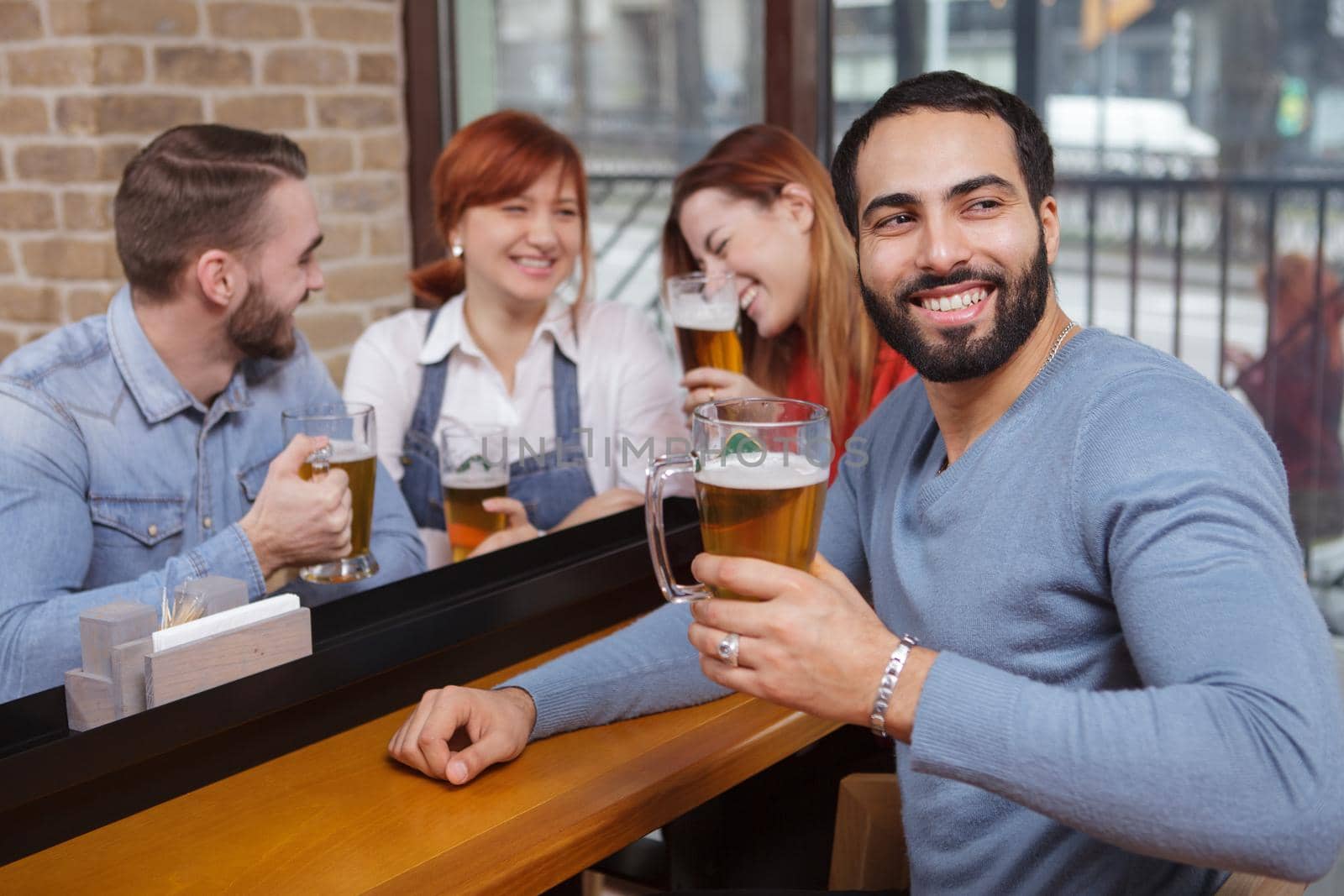 Handsome man looking away, enjoying his beer with a group of friends, copy space. Friendship, togetherness concept