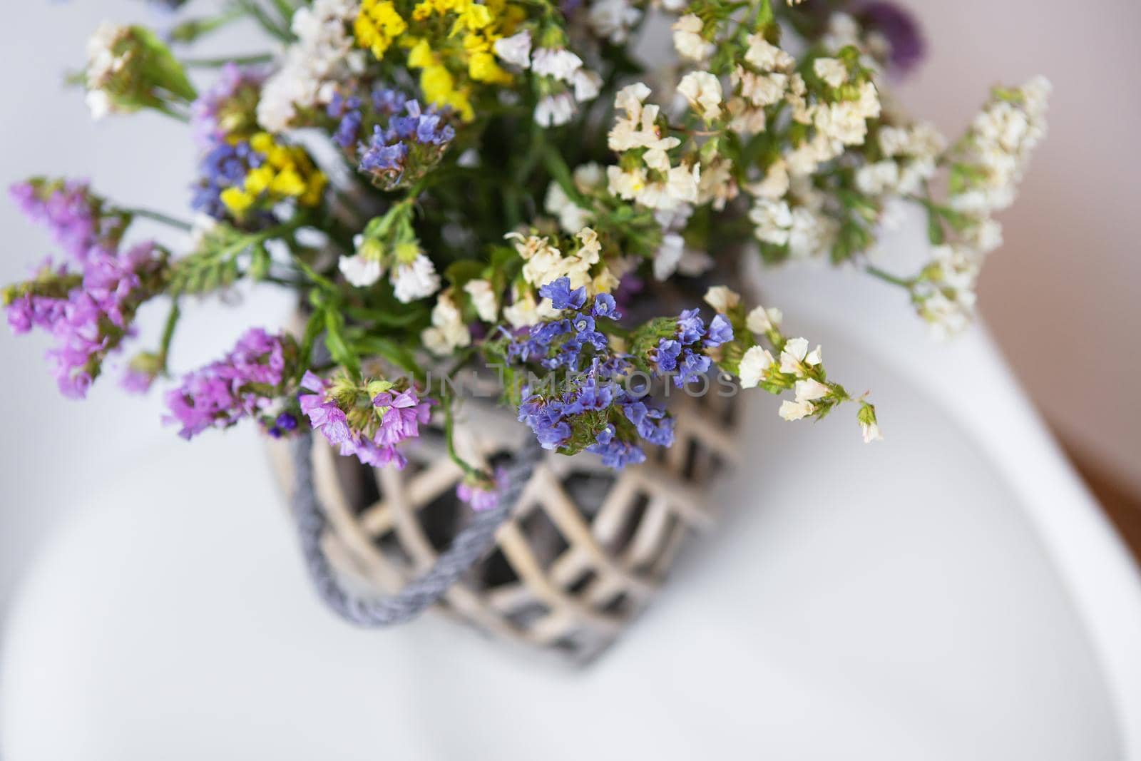 Dried flowers in a wooden vase stands on a white chair, copy space. Place for an inscription