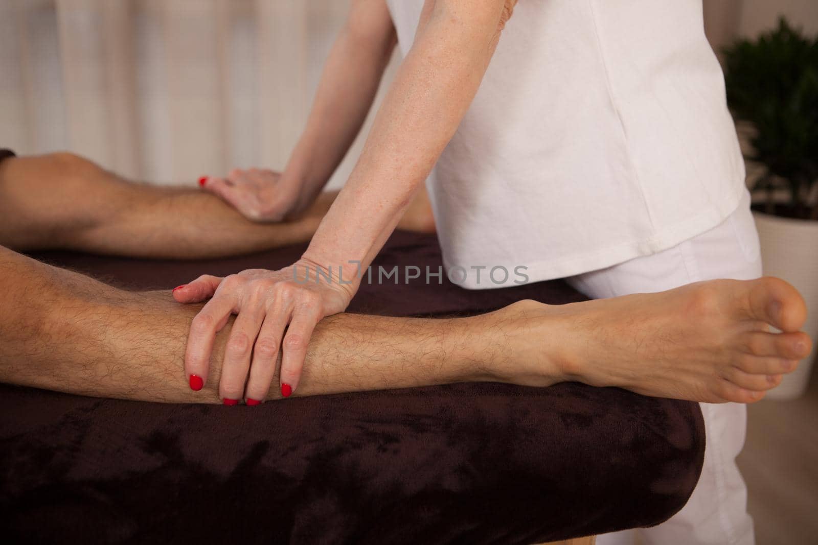 Unrecognizable female masseur massaging legs of a man