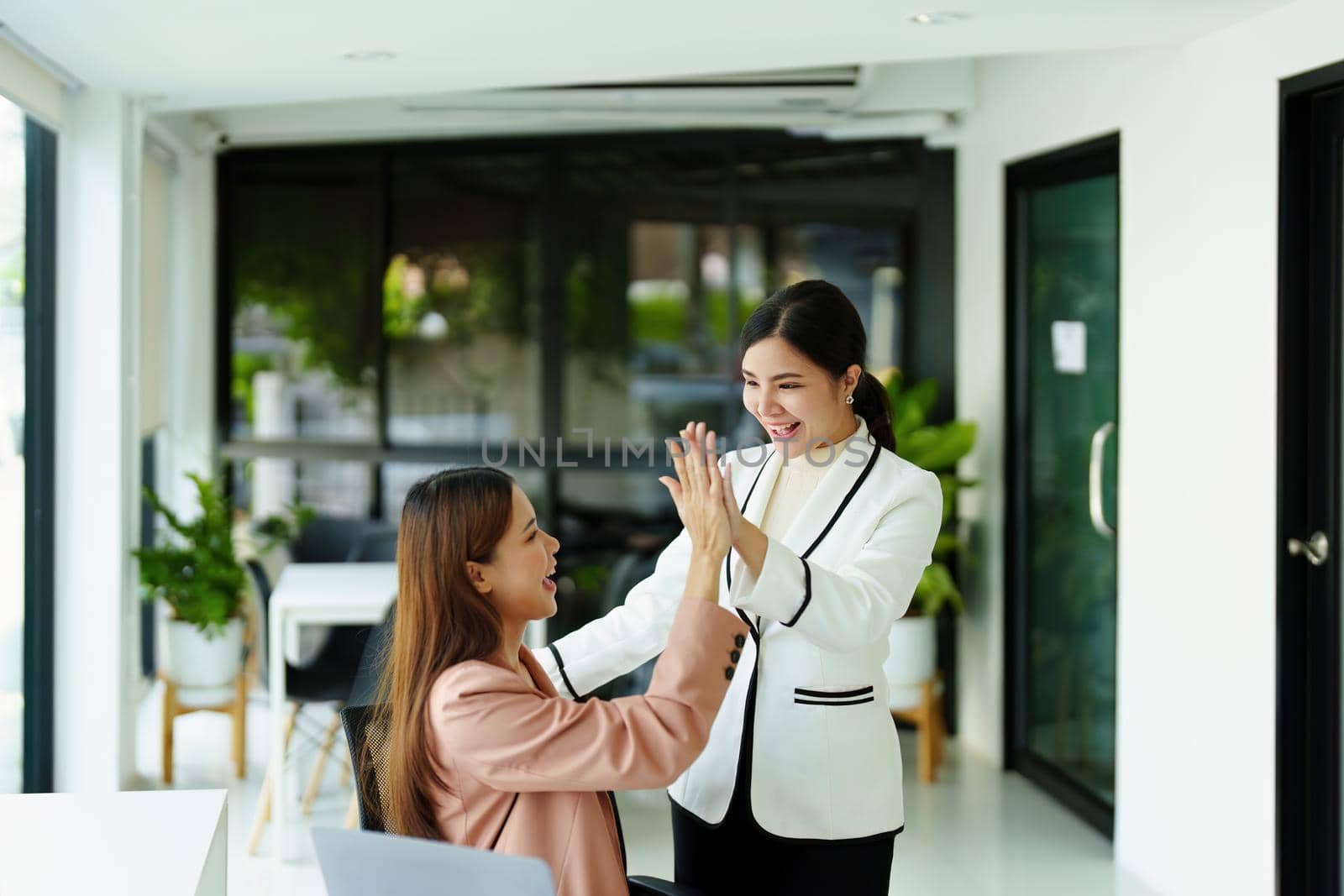 two female employees posing together after sales hit their targets. by Manastrong