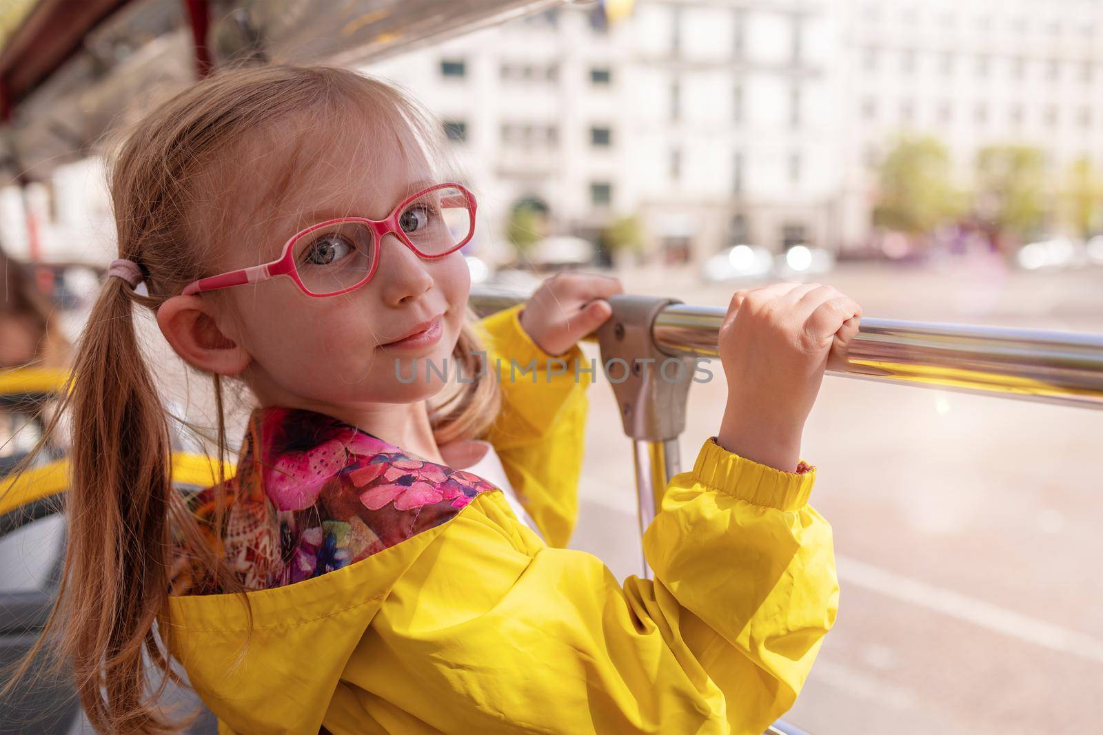 A little blonde girl of European appearance in eyeglasses. The child rides in a school bus, looks at the camera and smiles. Children's health concept. vision problems, astigmatism, nearsightedness