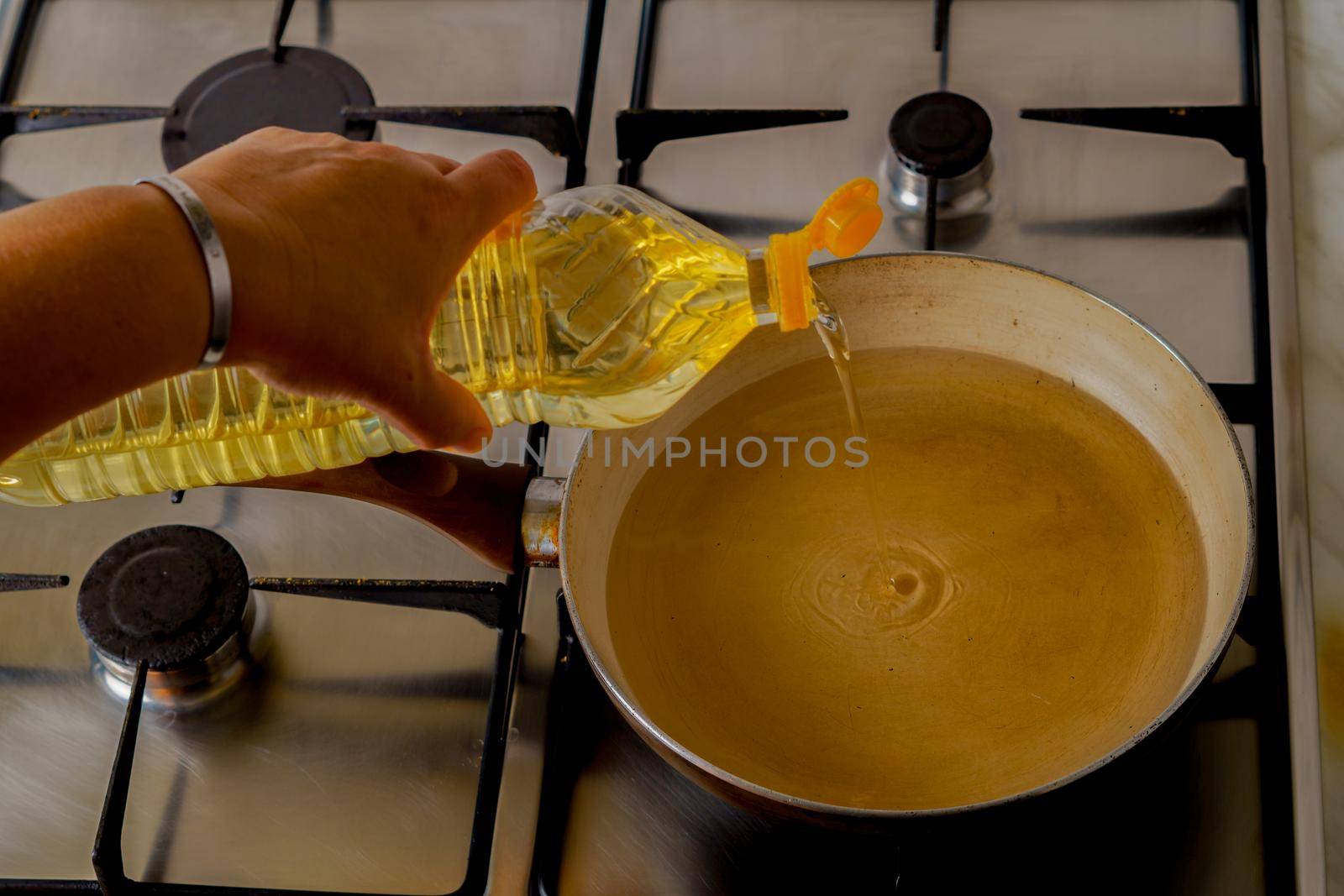 woman's arm pouring oil with a bottle into a frying pan in the kitchen of her house