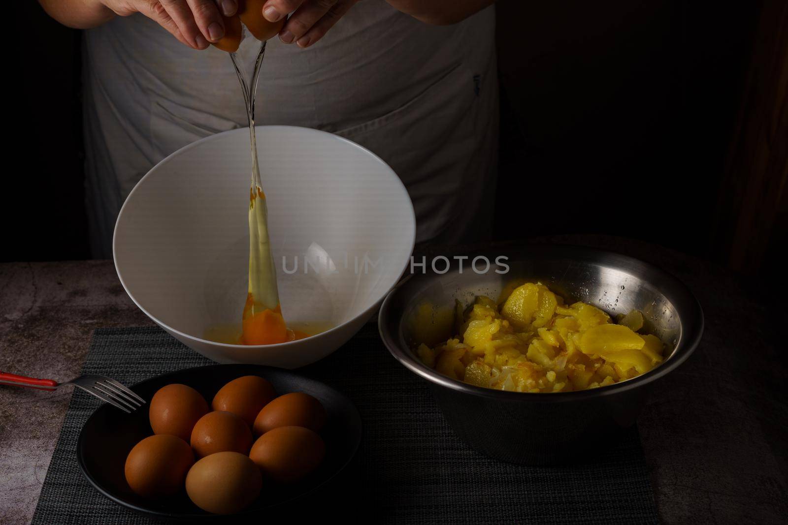 woman in white apron cracking eggs in a bowl by joseantona
