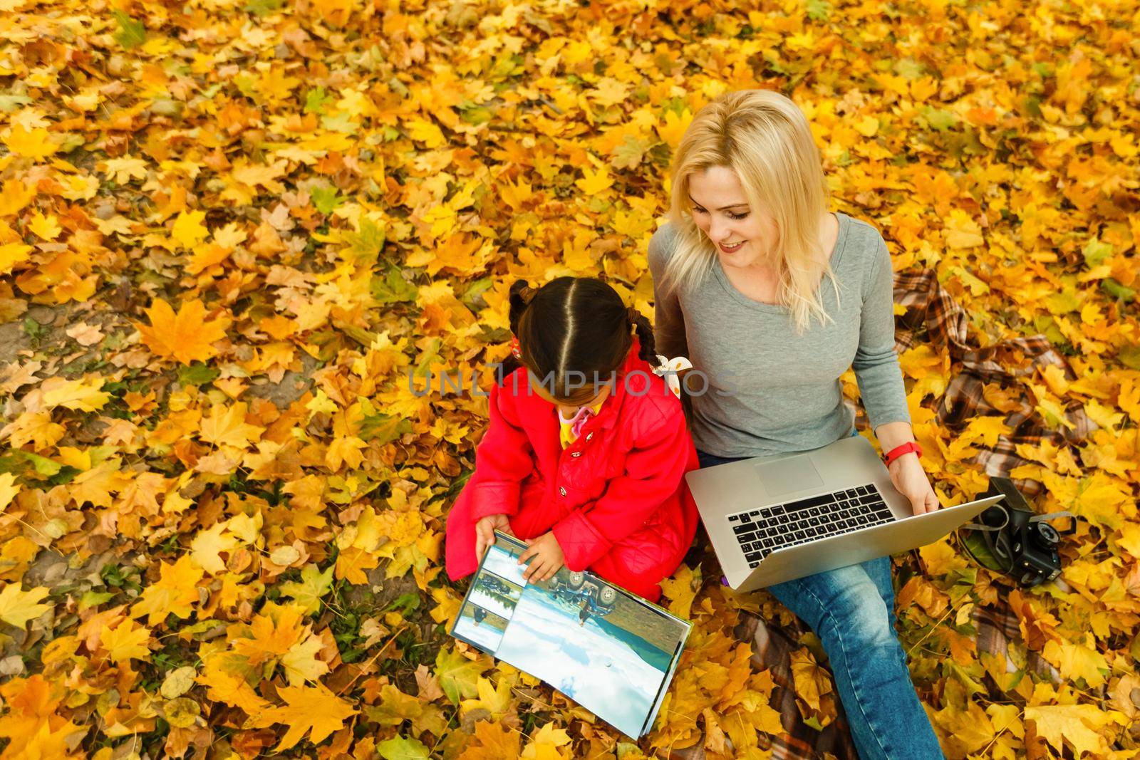 mother and daughter work on laptop outside in autumn