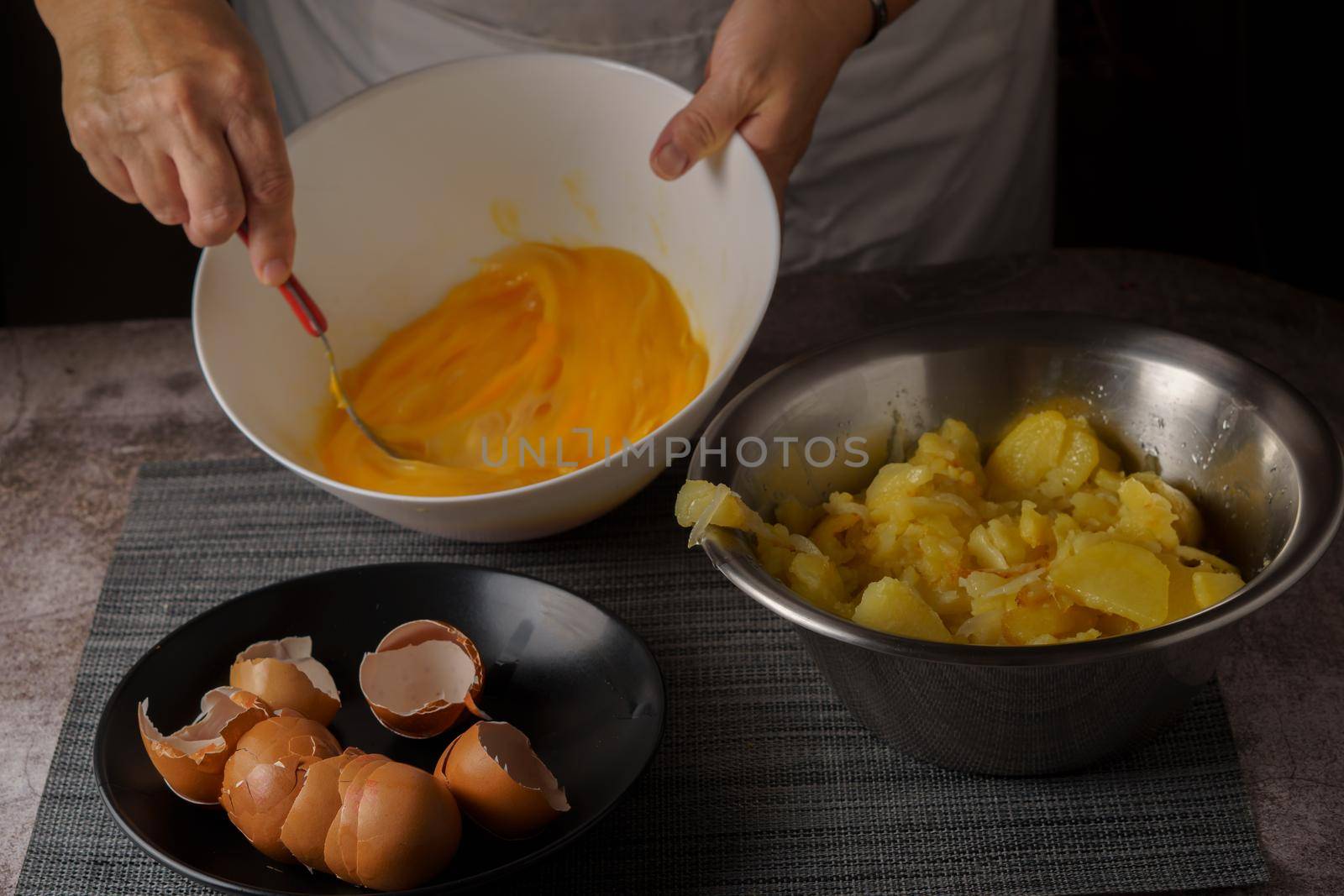 woman in white apron beating eggs in a bowl with the ingredients for a potato omelet