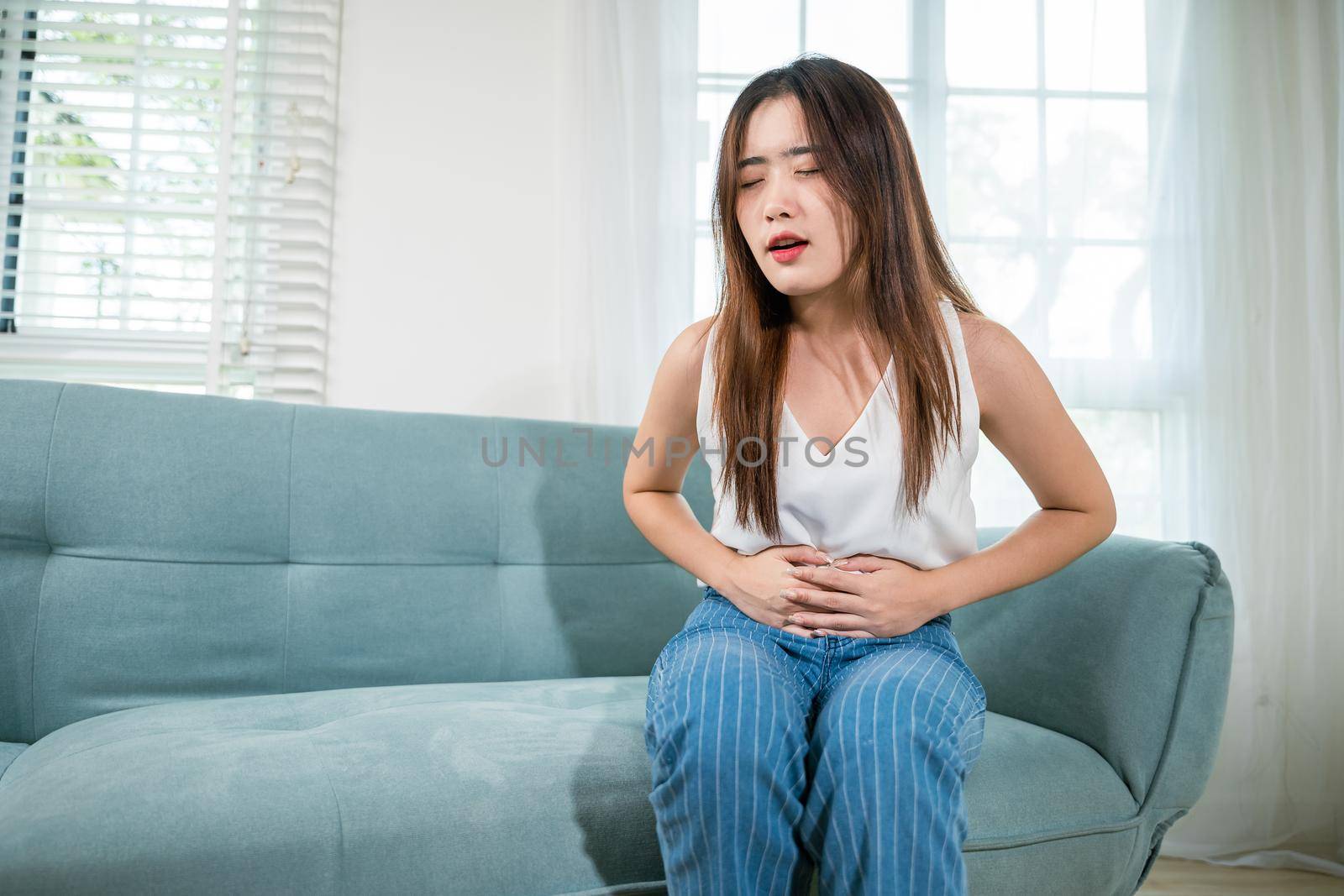 Asian young woman unhappy hands holding on stomach suffering from abdominal pain by Sorapop