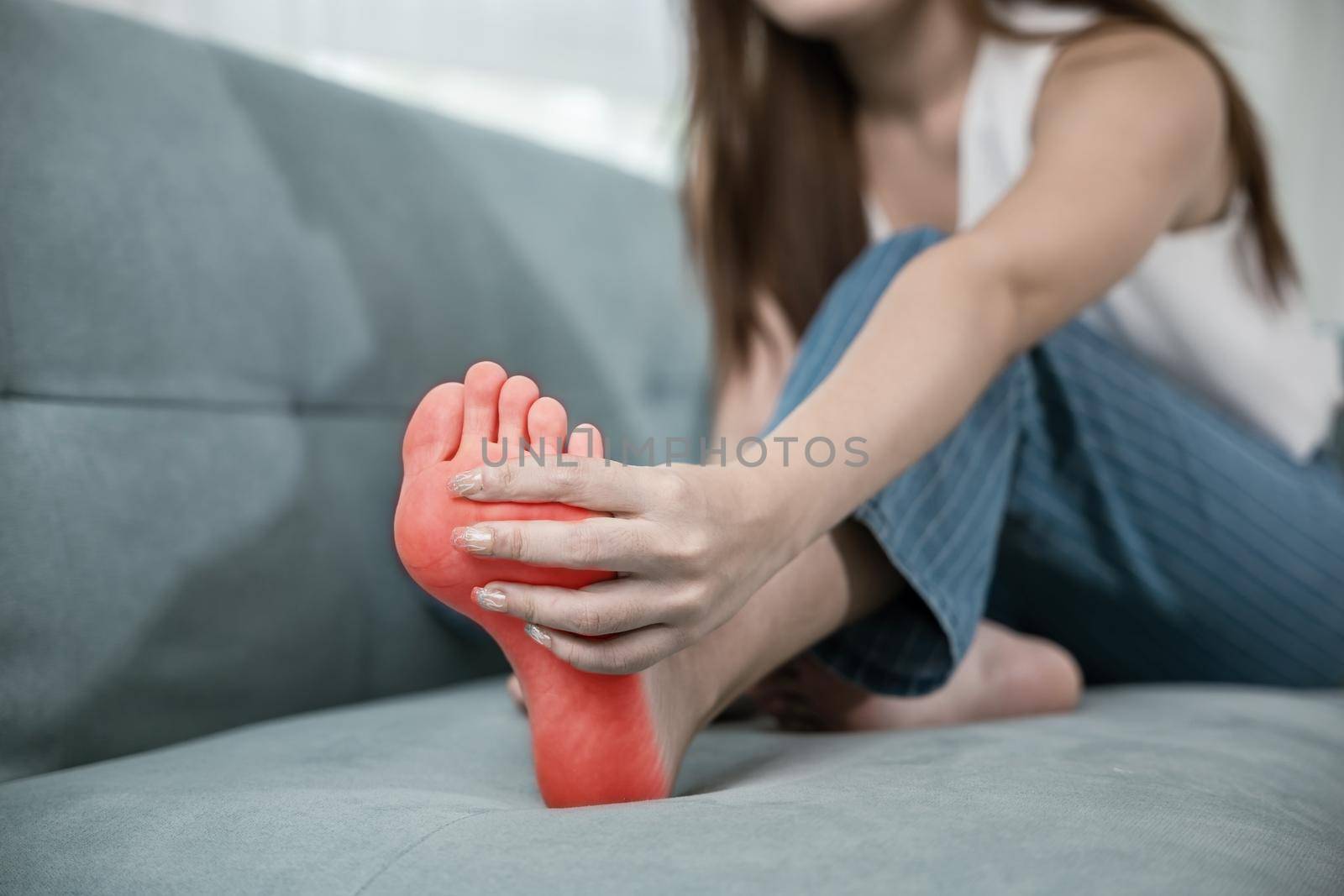 Asian young woman sitting on sofa holding her feet and stretch muscles have symptoms by Sorapop