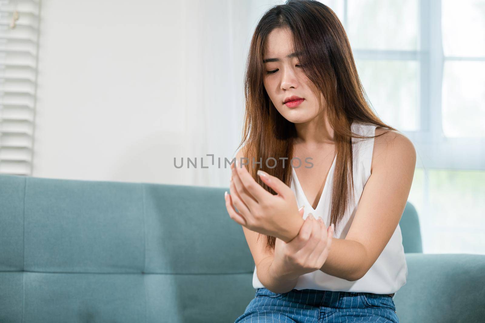 Closeup hand. Asian young woman sitting on sofa holds suffering her wrist at home, female hand injury feeling joint pain, performing self-massage, Health care and medical concept
