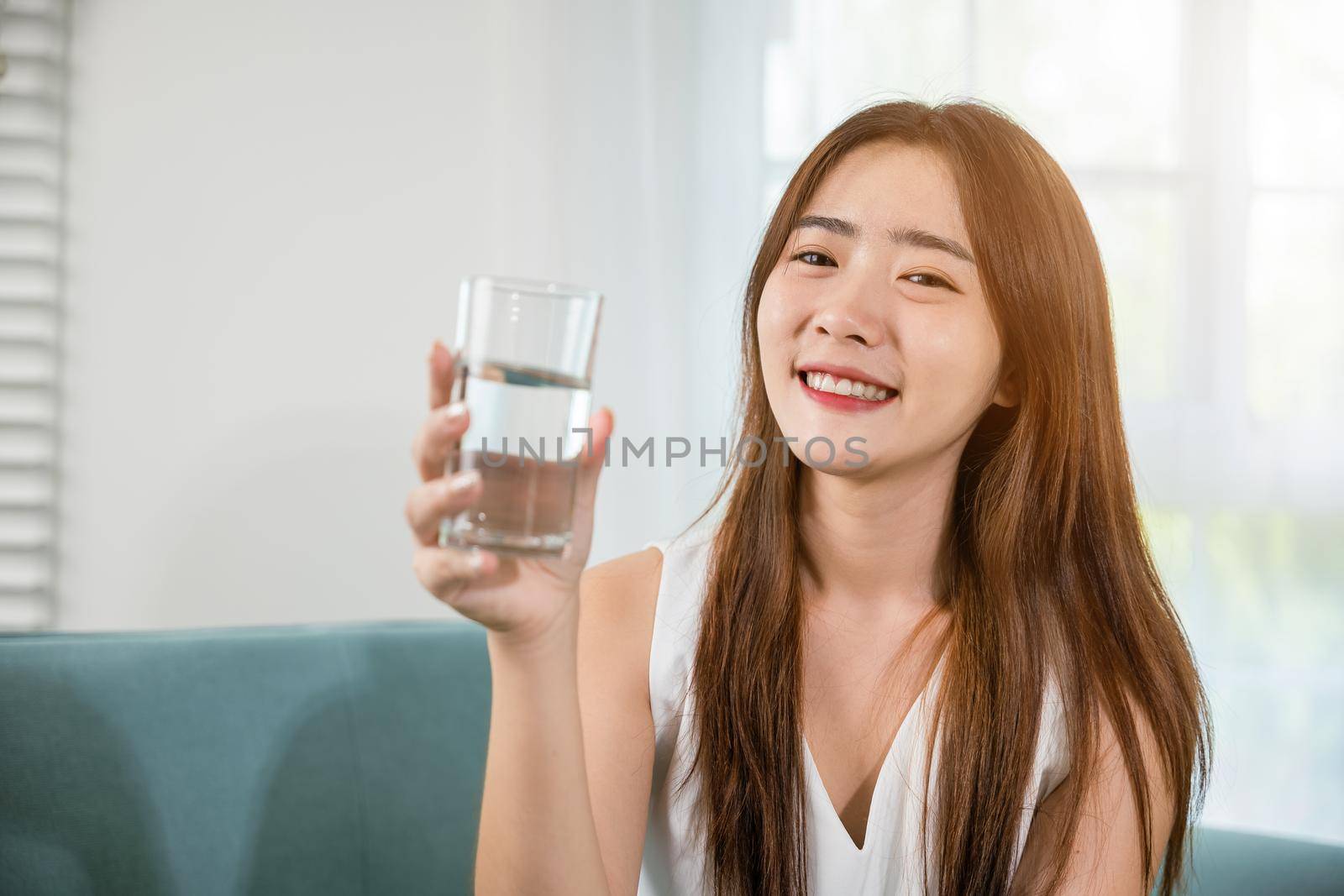 Portrait of Asian young woman holding drinking nature water on hand at home, Happy smiling female beauty with water glass for drink in living room, Healthy lifestyle