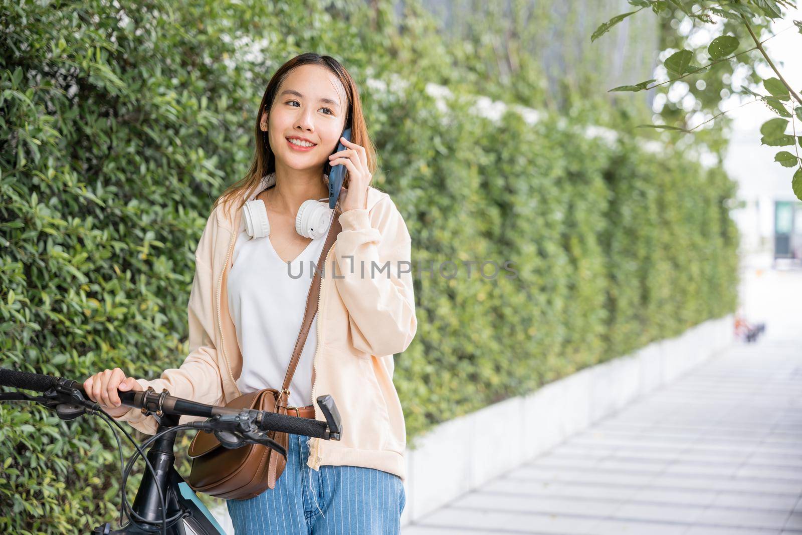 Happy female smiling walk at street with her bike on city road and cellphone with mobile phone, Asian young woman commute on smartphone with bicycle on summer in park countryside outdoor, travel