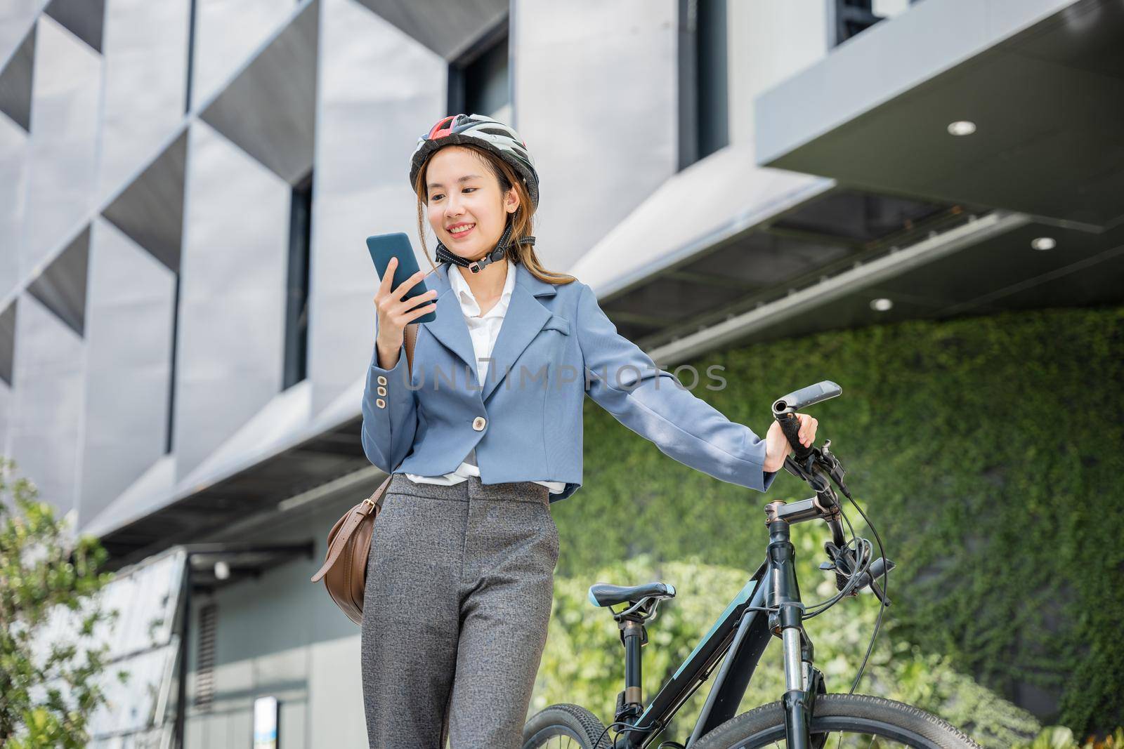 Asian smiling young woman with helmet hold mobile smart phone talk with business during go to office work at street with bicycle, Eco friendly, Lifestyle business female commuting outside in morning