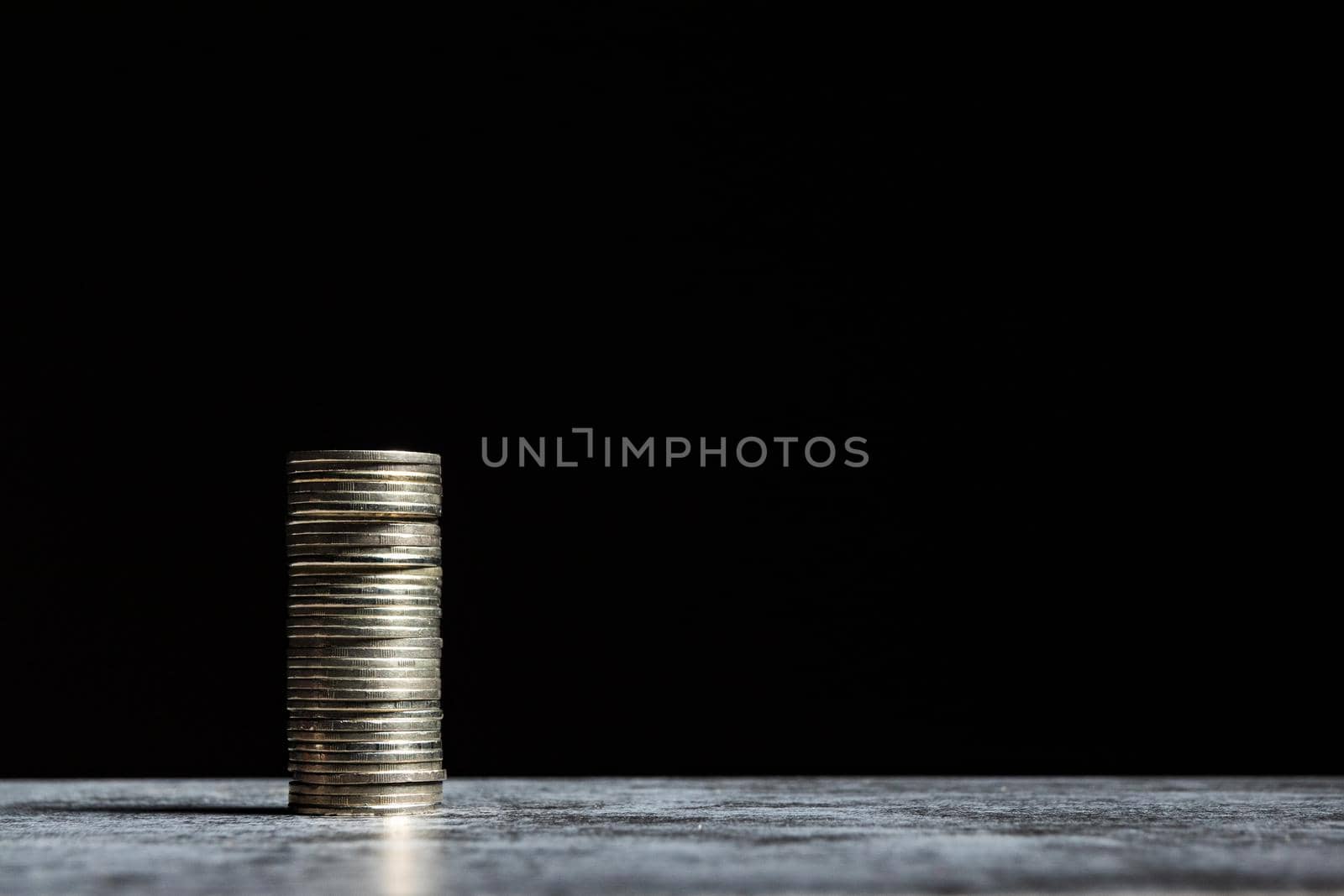 Stack of coins on grey table and black background. Start-up capital concept with copy space.