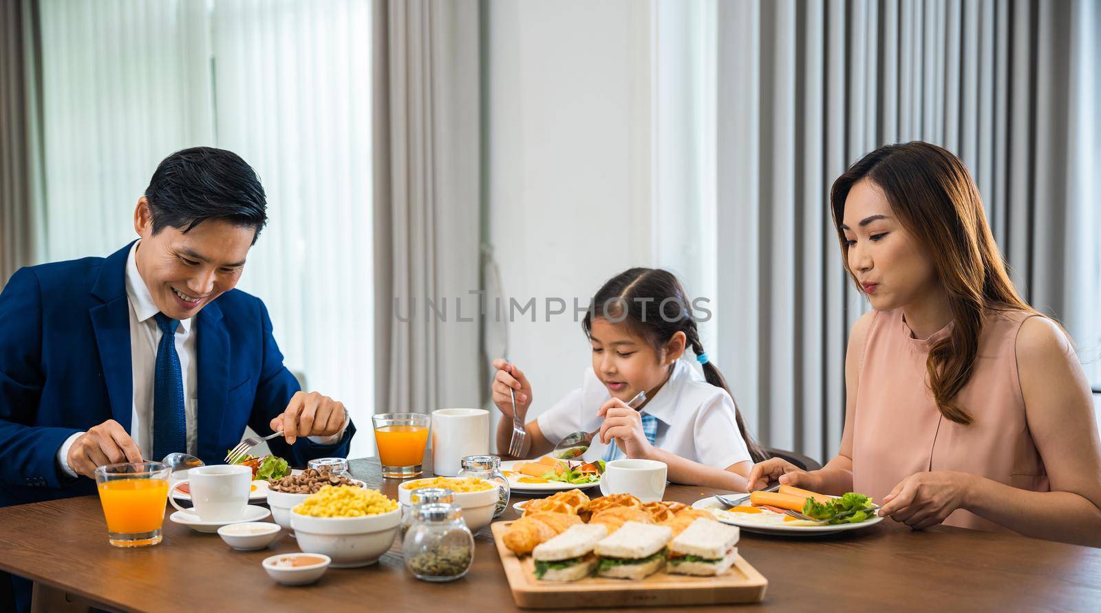Asian family father, mother with children daughter eating healthy breakfast food on dining table kitchen in mornings together at home before father left for work, happy couple adult family concept