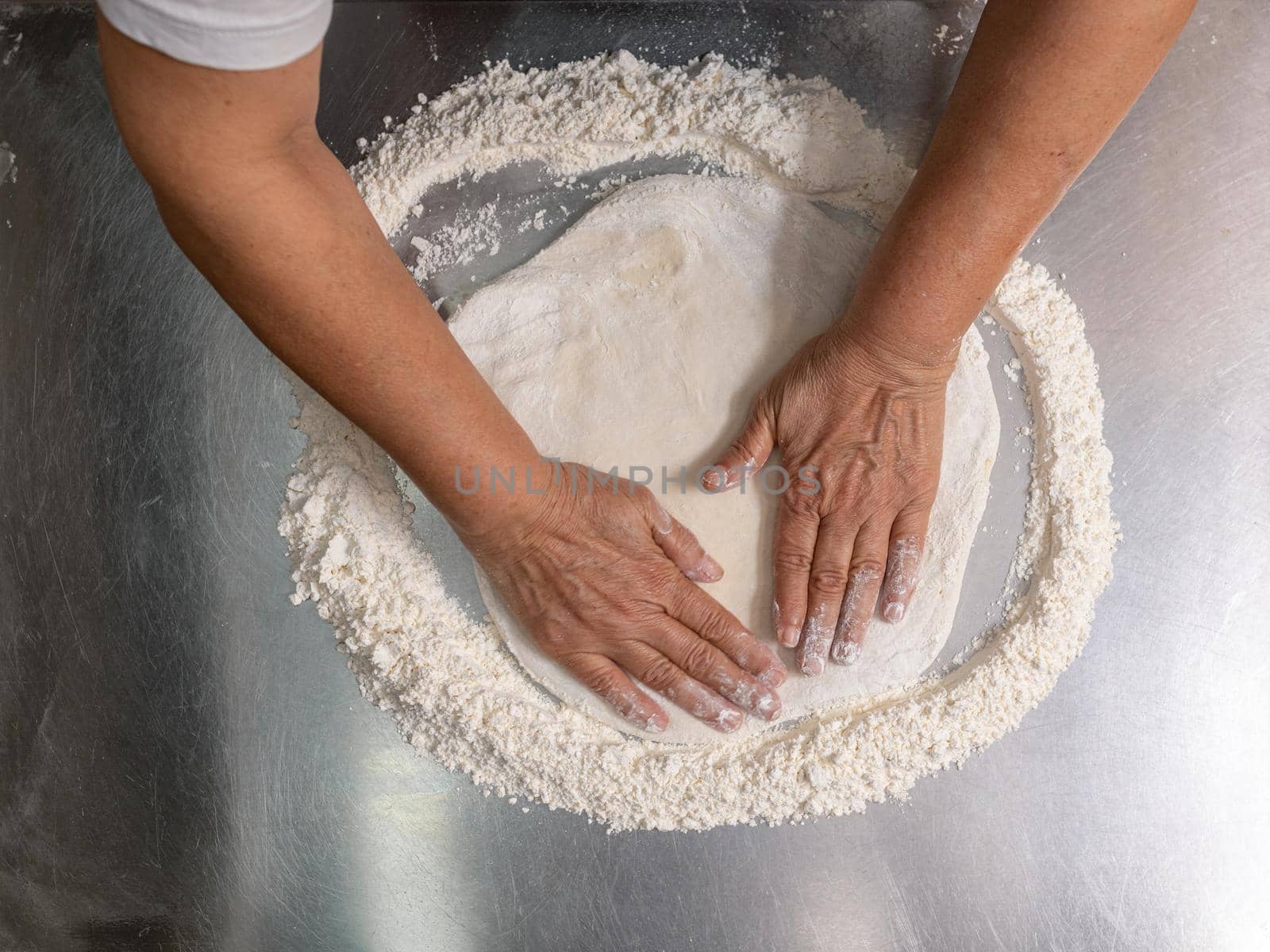 Woman making pizza dough on stainless steel counter