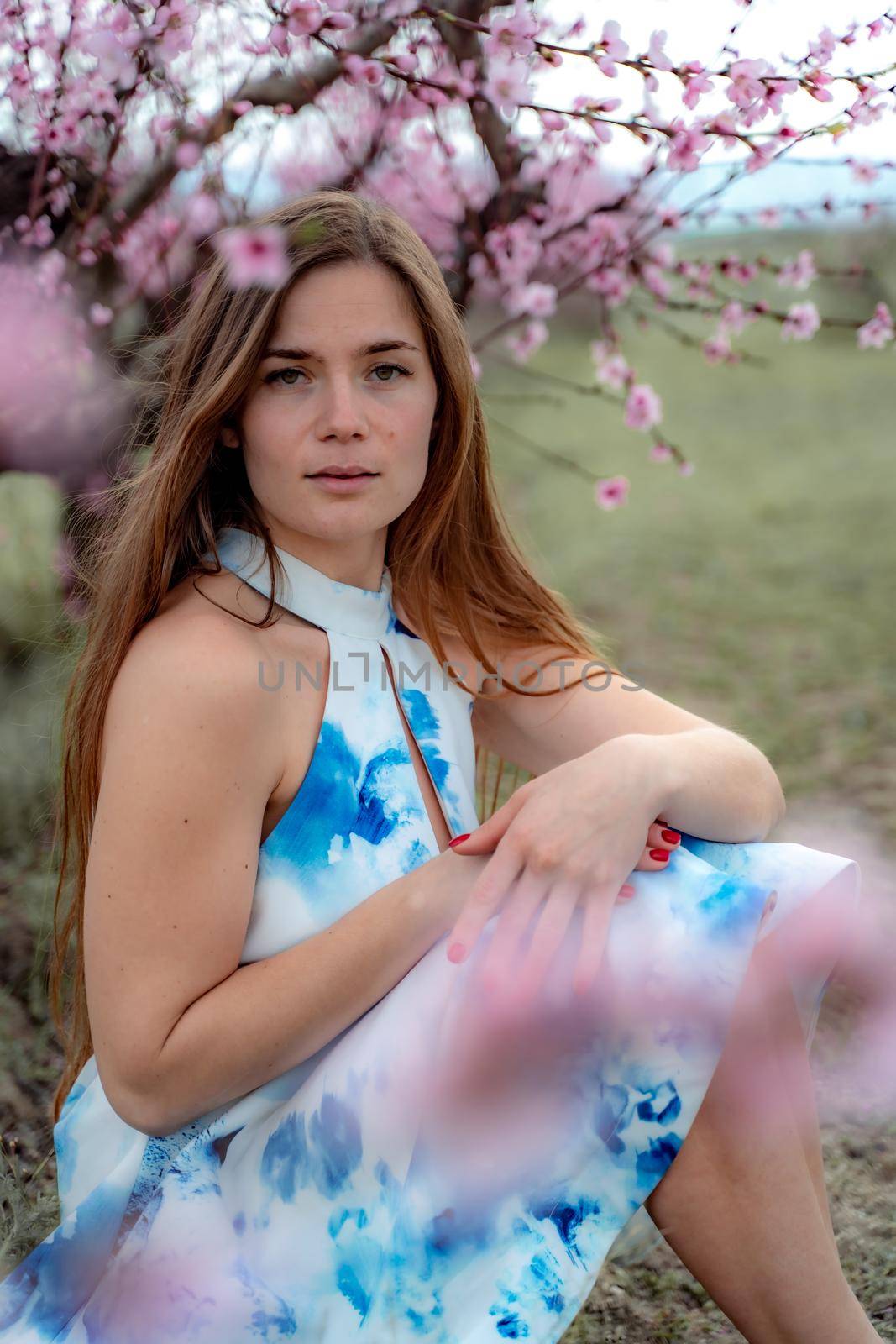 Young beautiful woman in blue dress and long hair is enjoying with blossoming peach trees by Matiunina