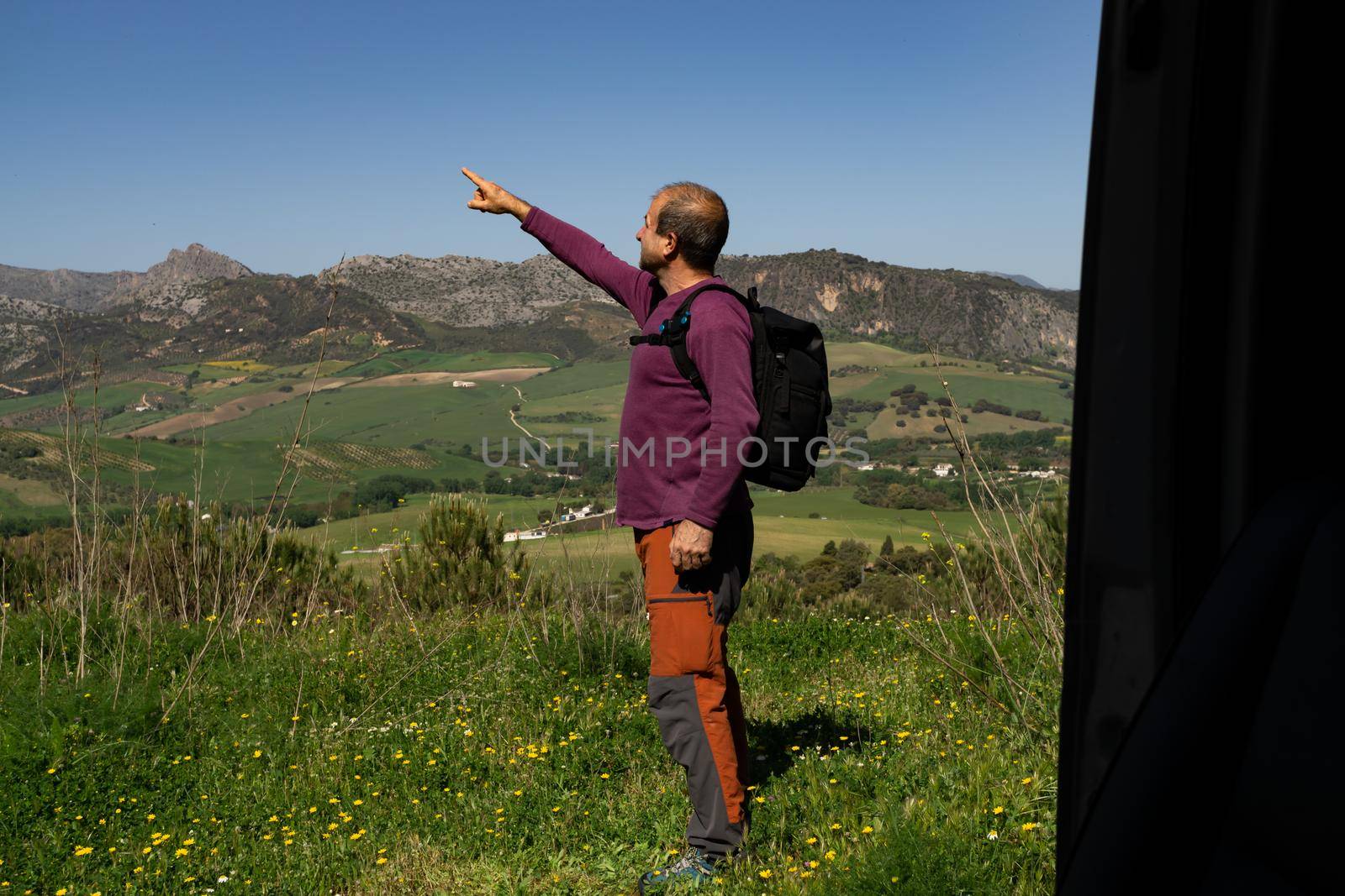 man with backpack on mountain pointing to the horizon mountain landscape with blue sky seen from inside his van