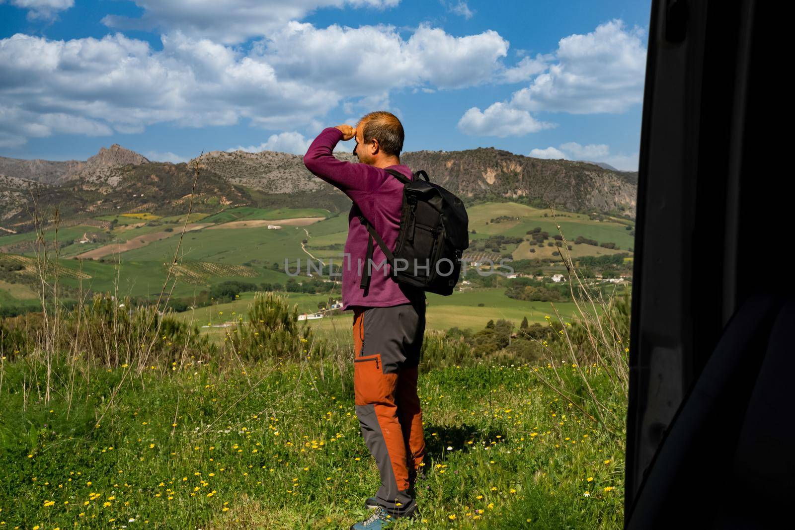 man with backpack observing the horizon mountain landscape in the background and cloudy sky seen from inside his van