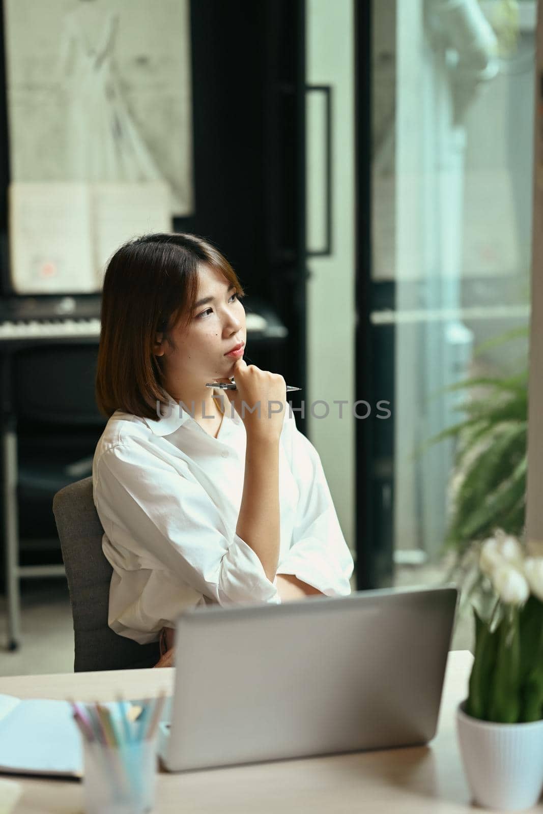 Thoughtful woman entrepreneur sitting at her workplace and looking through window, dreaming of success thinking of future business.