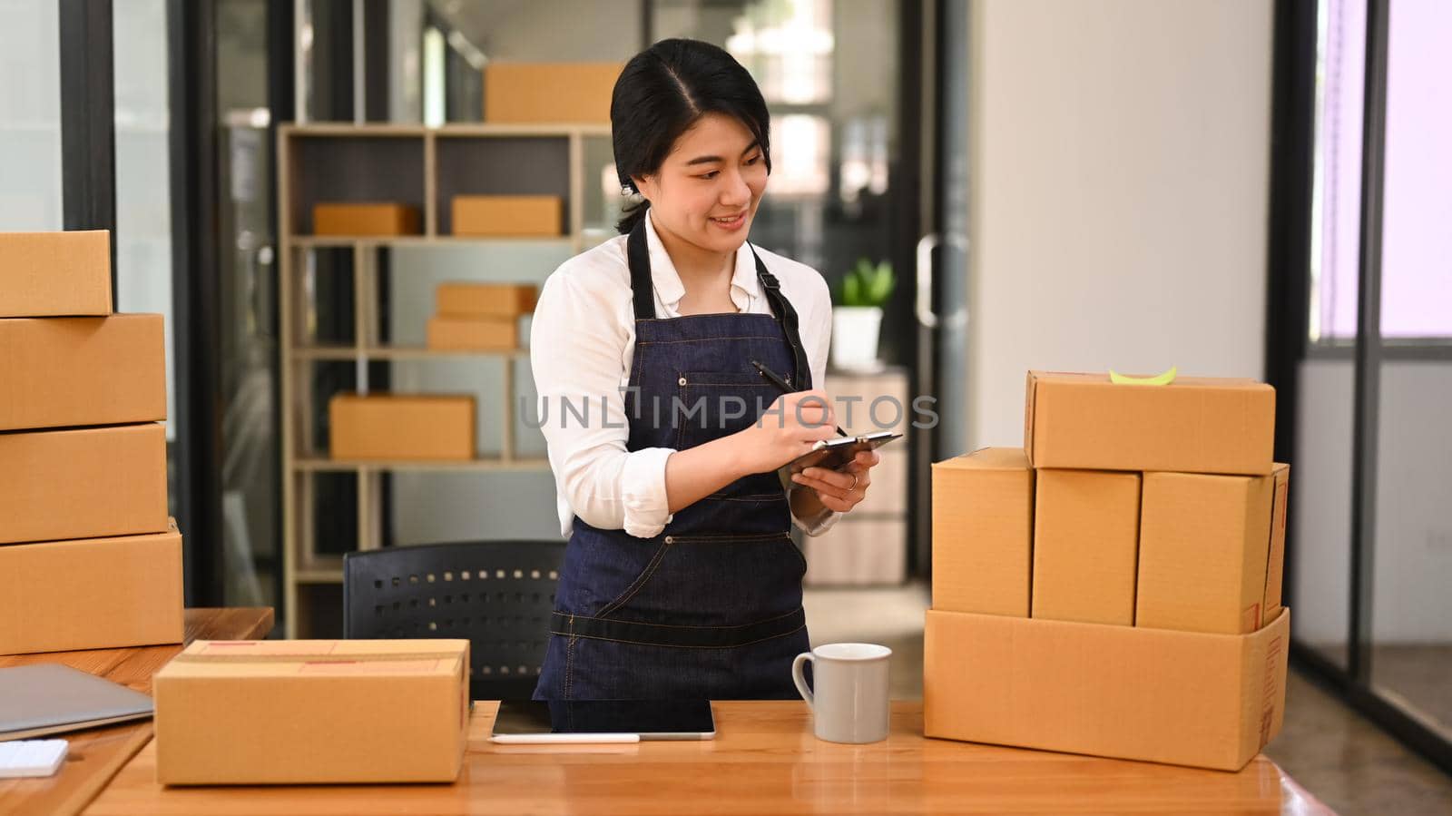 Smiling startup small business entrepreneur checking order and preparing parcel boxes for shipping to customer.