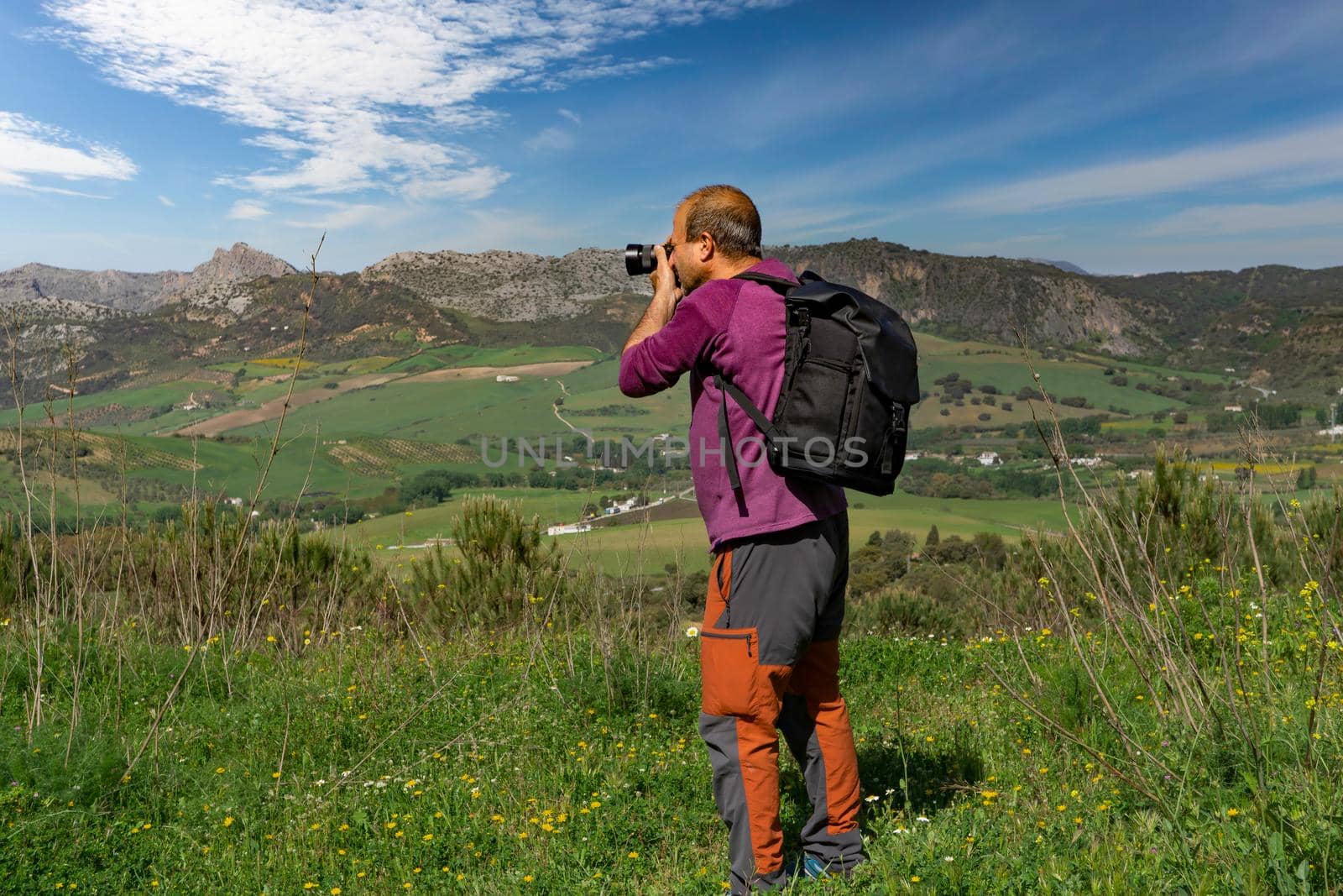 a man with a backpack on the mountain photographing the landscape on a cloudy sky day