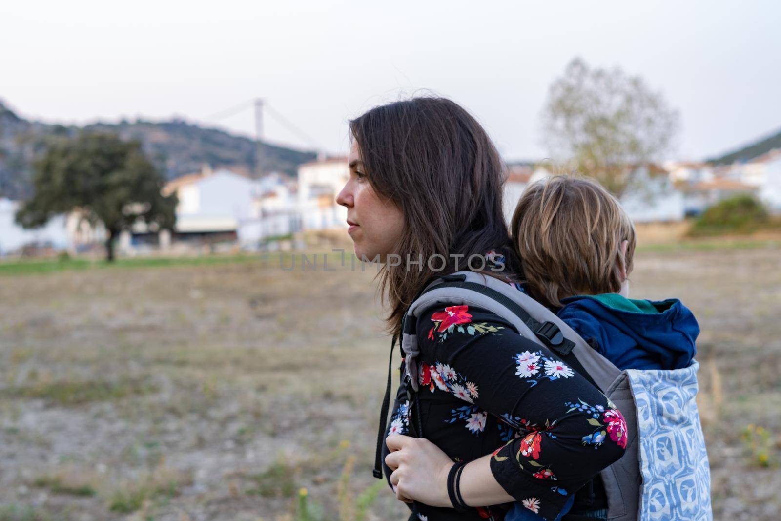 Young mother with her toddler kid boy on back in ergonomic baby carrier in autumn nature. Active mother concept