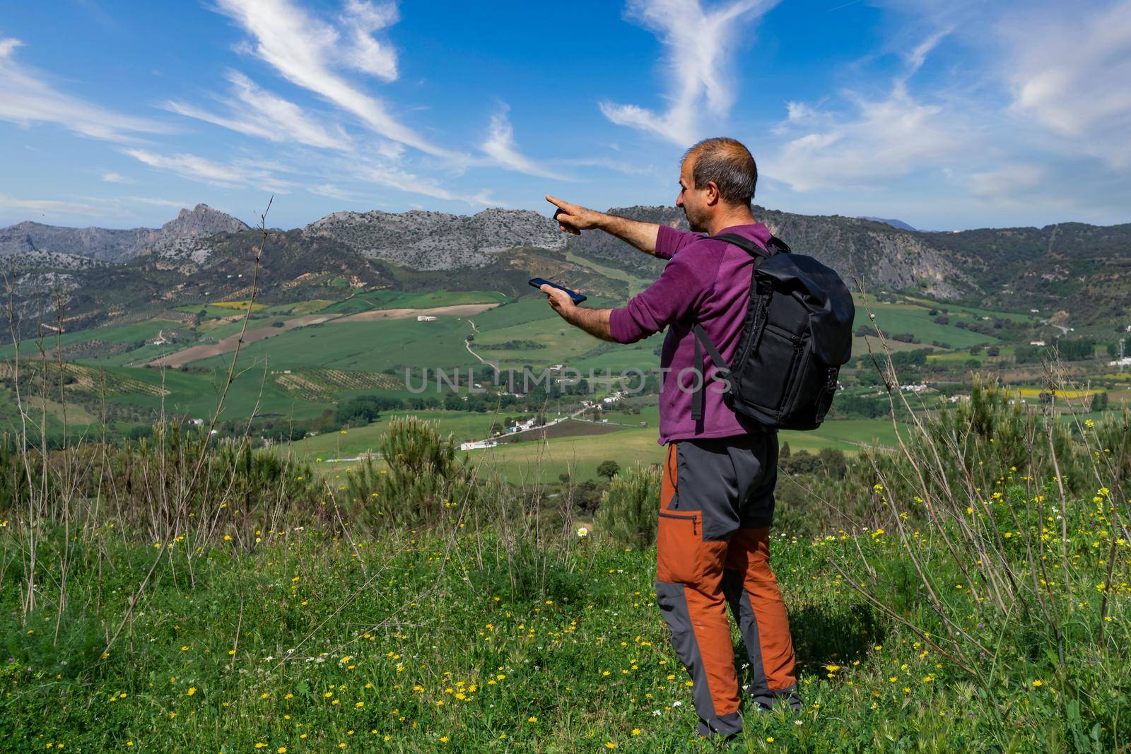 man with backpack man orienting himself in the mountains with his mobile phone, mountain landscape in the background and cloudy sky