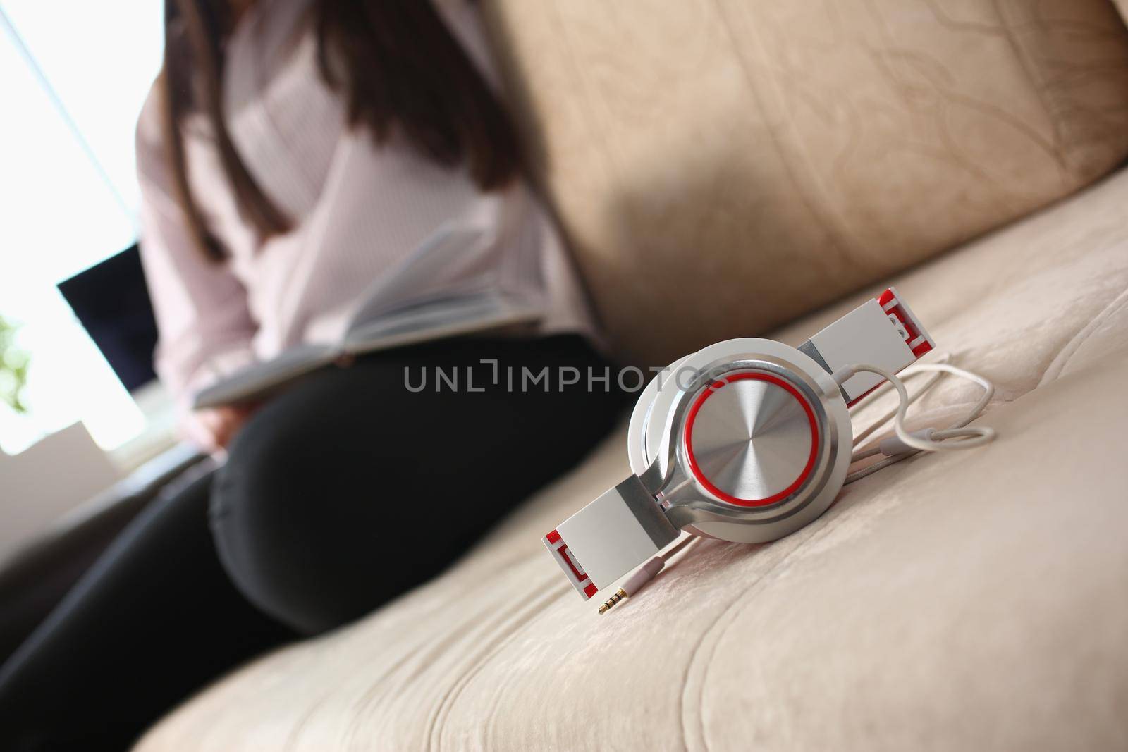 Fashionable white red headphones lie on the sofa in background person sits. Headphones and headsets for home