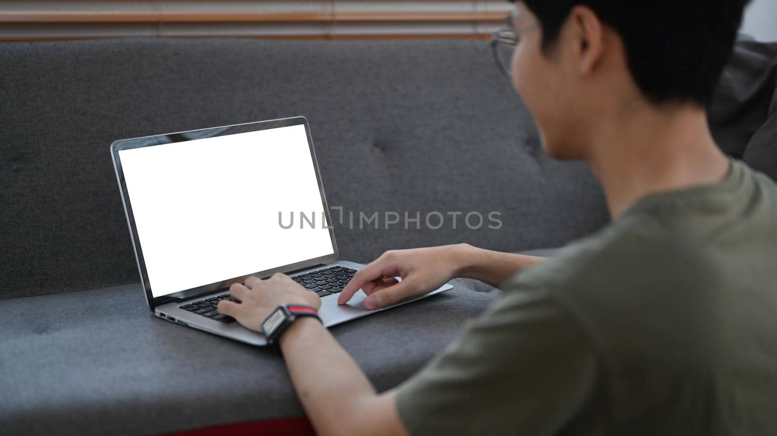 Rear view of asian man sitting in living room and reading email or surfing internet on laptop computer.