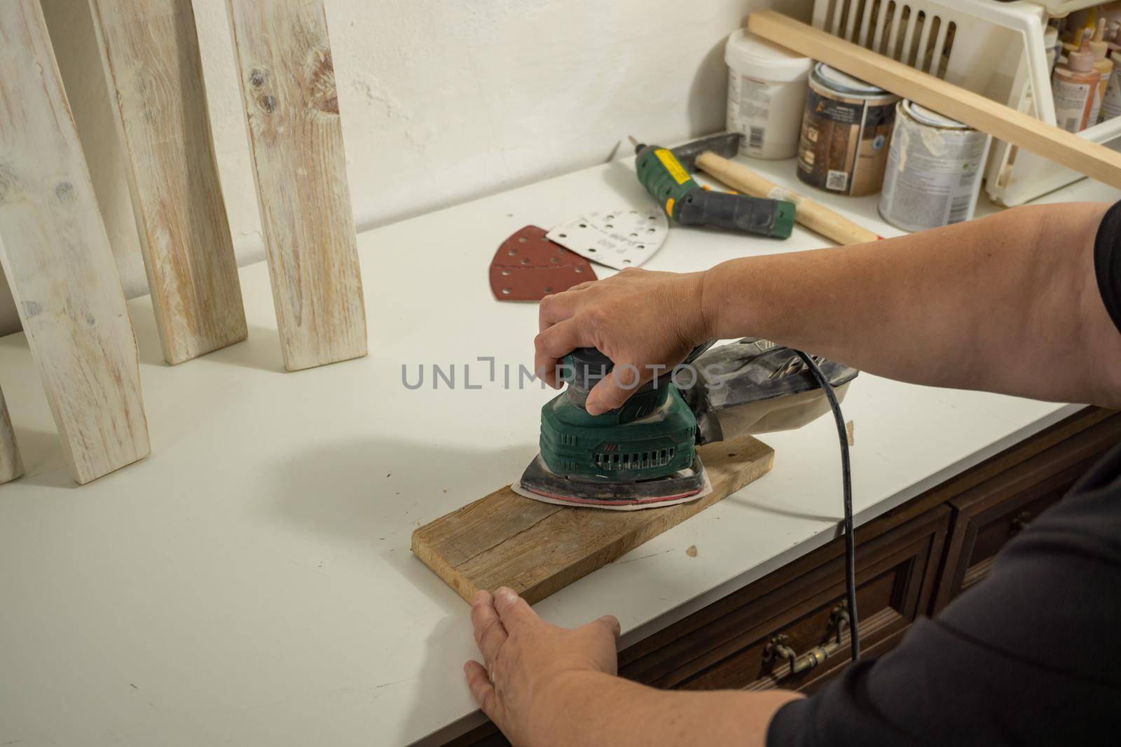 hands with electric sanding machine sanding wood in a workshop