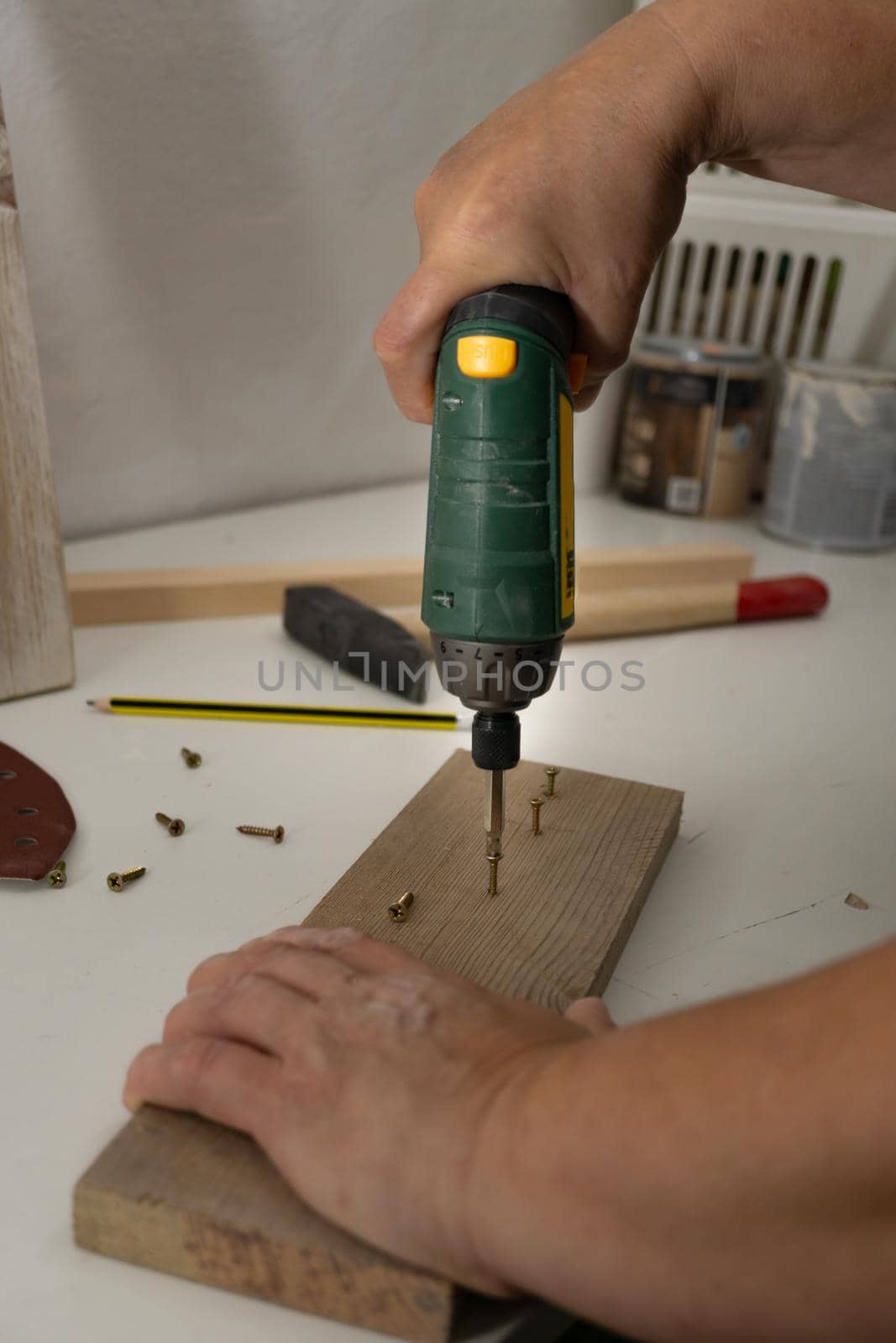hands with electric screwdriver screwing screws into wood