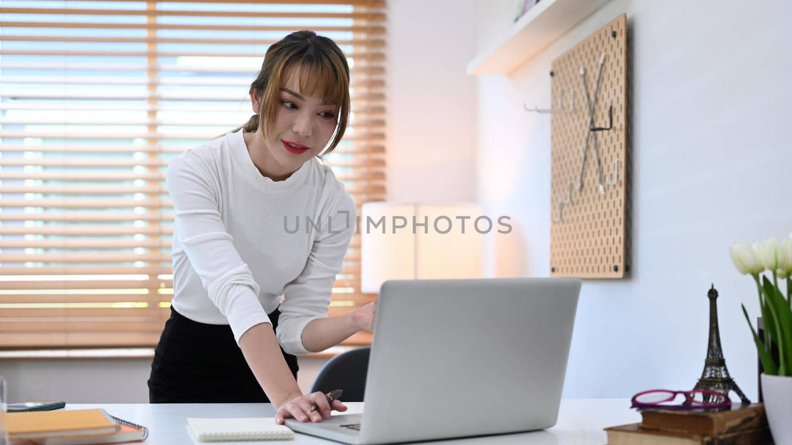 Charming young creative woman working online or making video call with laptop computer at home office.