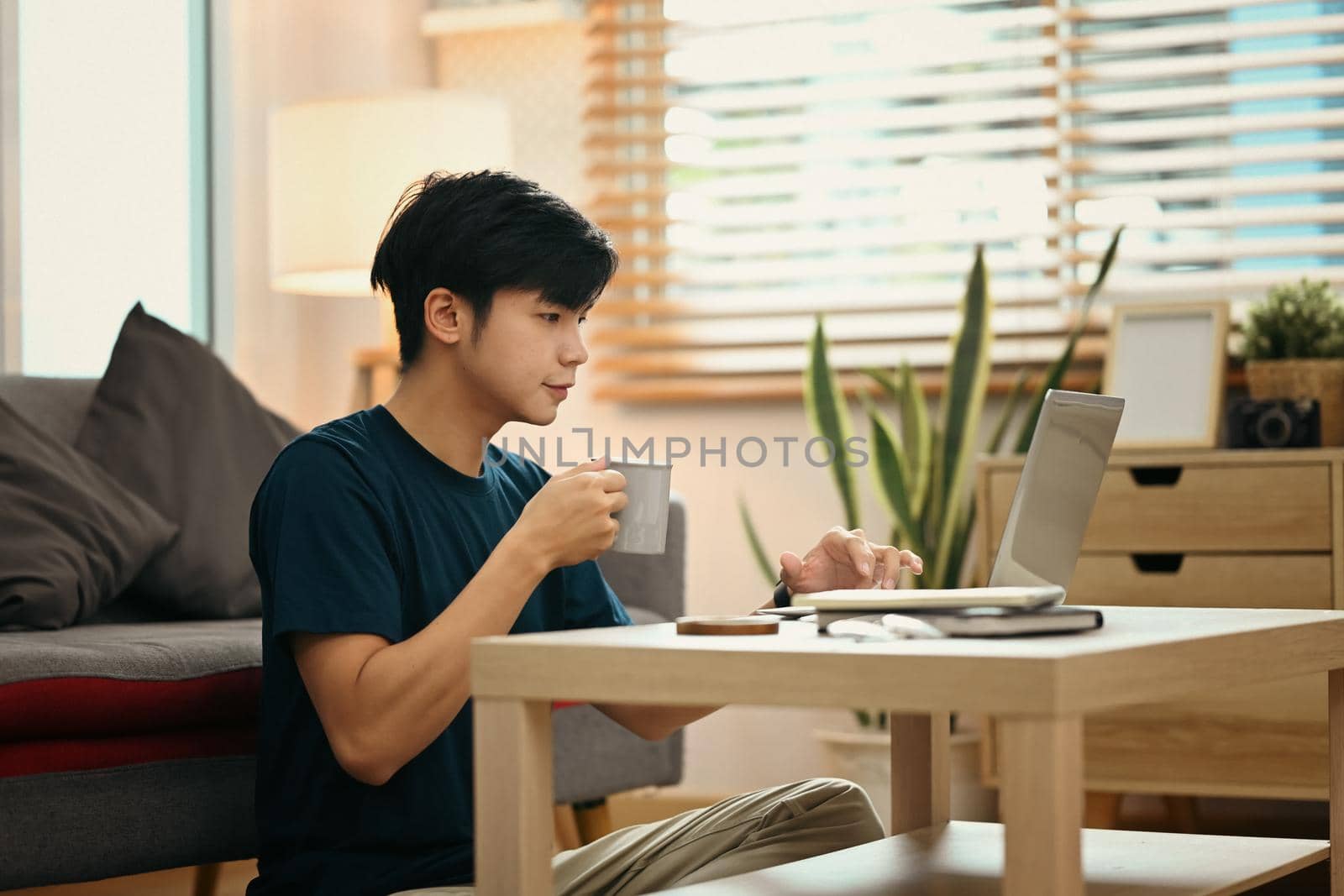 Casual man drinking coffee and reading email on the screen of a laptop while relaxing in comfortable home.