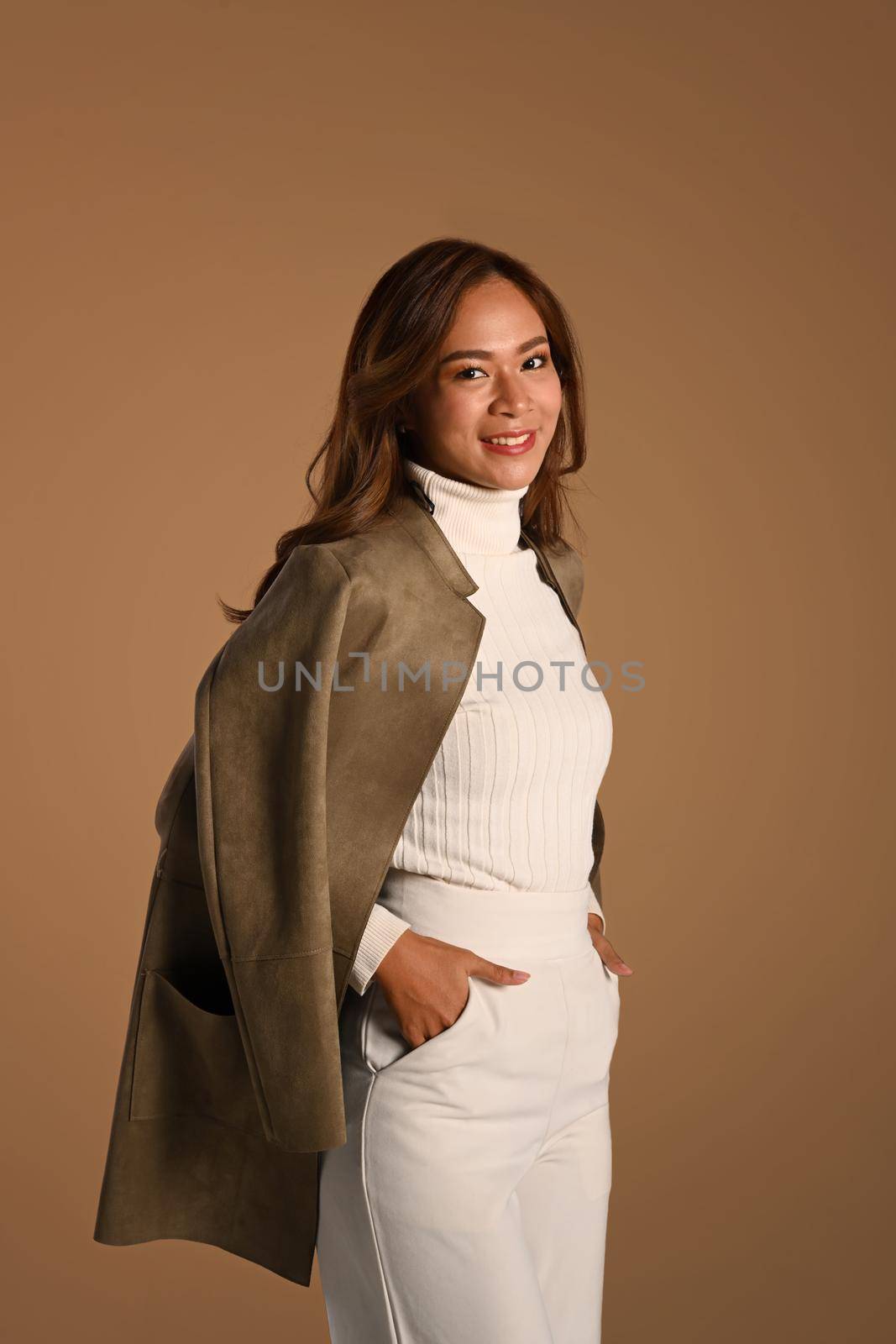 Elegant woman wearing trendy coat and holding hands in pockets standing on brown background. Autumn and Winter concept.