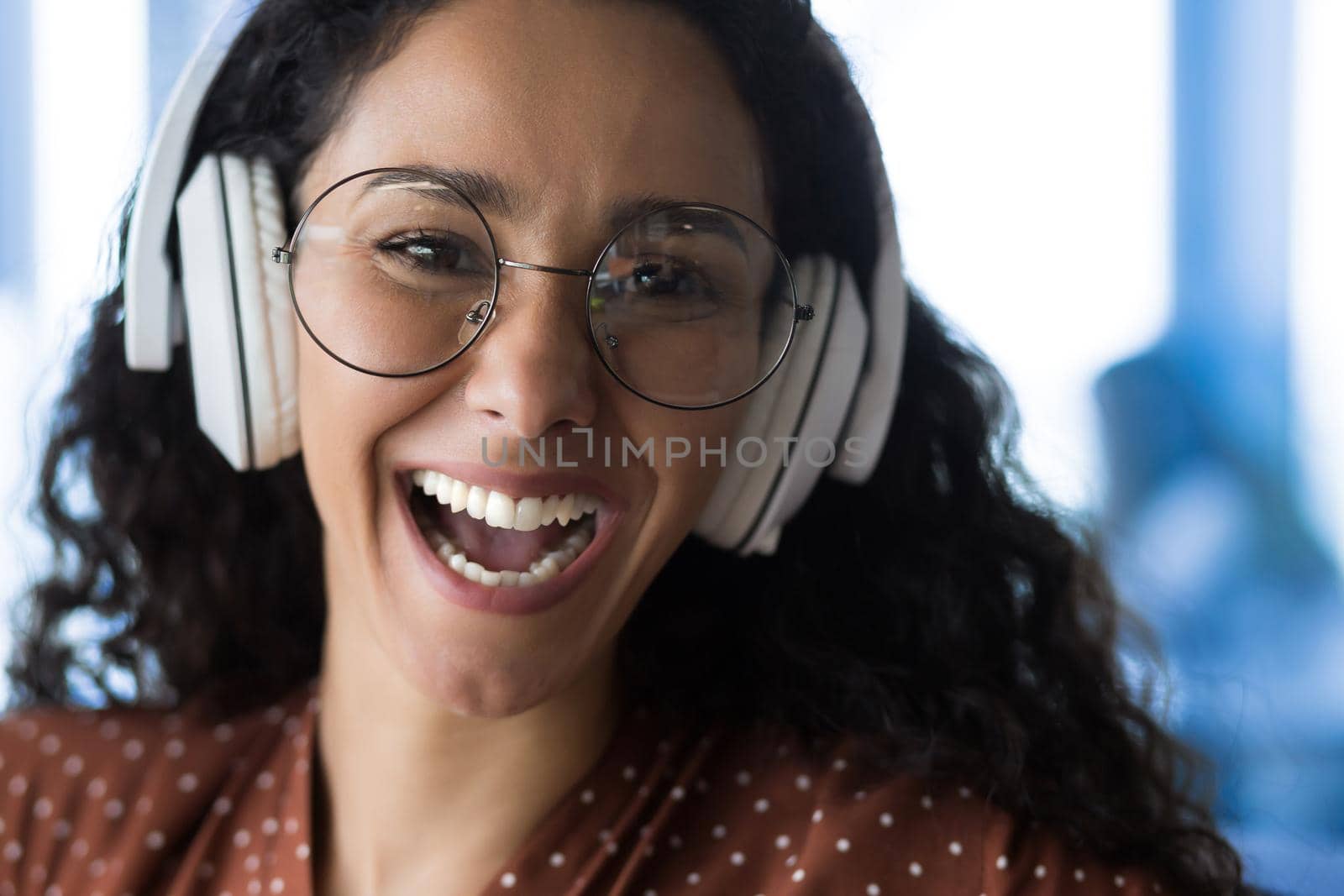 Close-up photo portrait of happy woman wearing glasses, smiling and happy listening to music in white headphones and looking at camera, selected focus