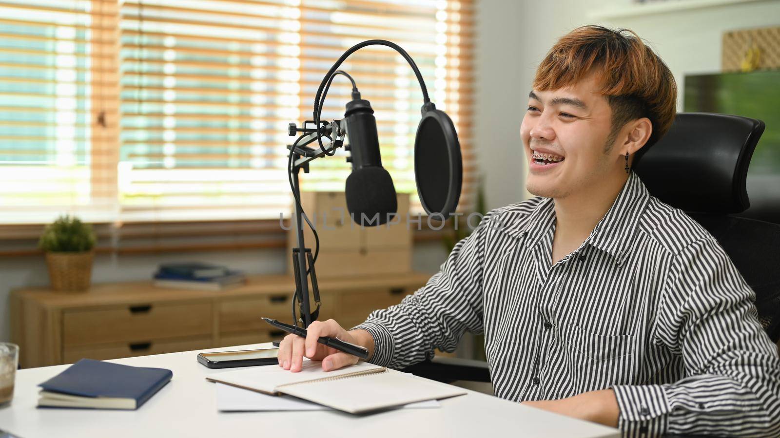 Cheerful Asian man using microphone while streaming audio podcast at home studio. Entertainment, podcasts and technology concept.