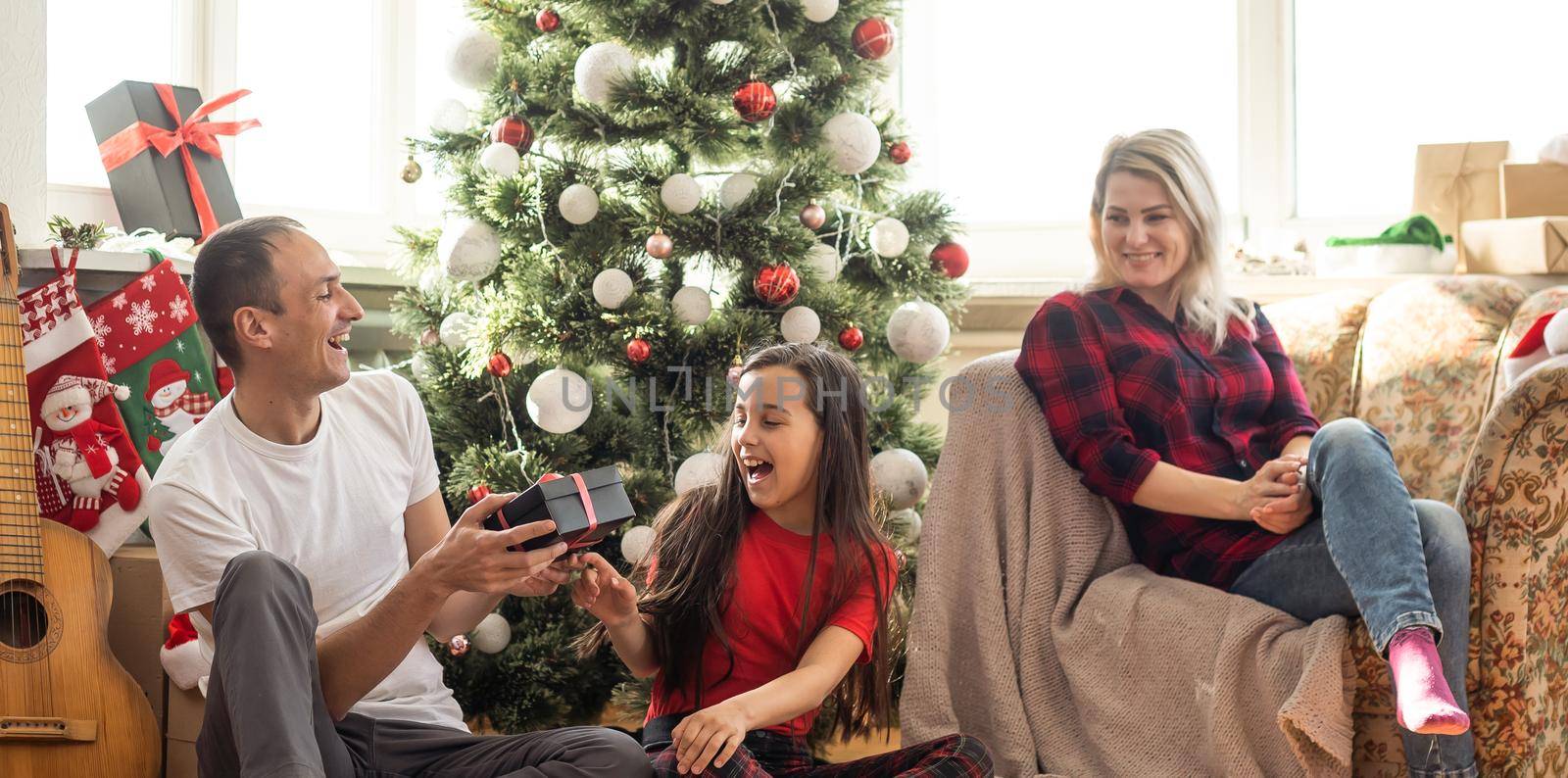 Happy family with cute daughter near Christmas tree together at home.