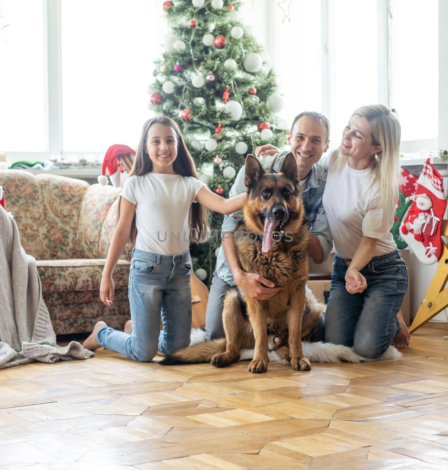 Merry Christmas and Happy New Year. Happy family with dog are waiting for the New Yearwhile sitting near beautiful Christmas tree at home. by Andelov13