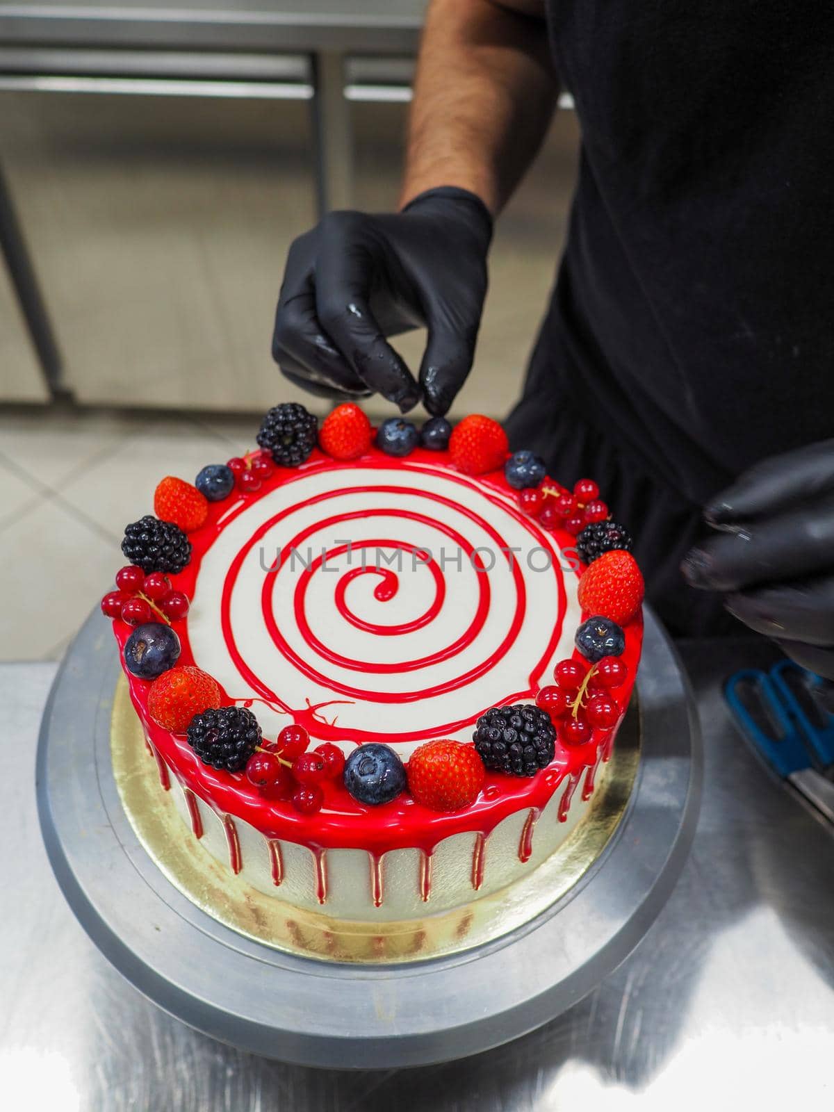 hand of chef toppig a choco cake with gold and berries in the lab