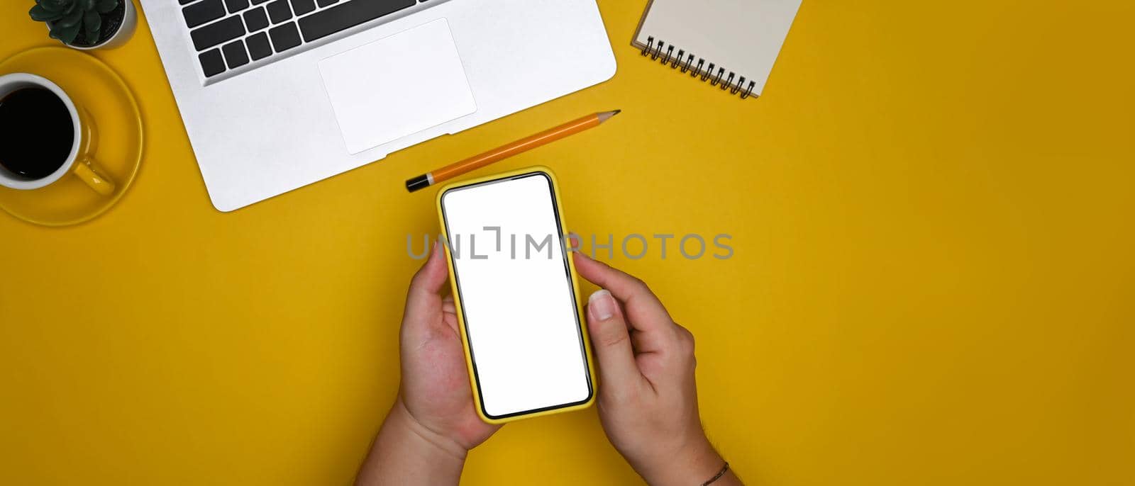 Above view man holding smart phone on yellow background.