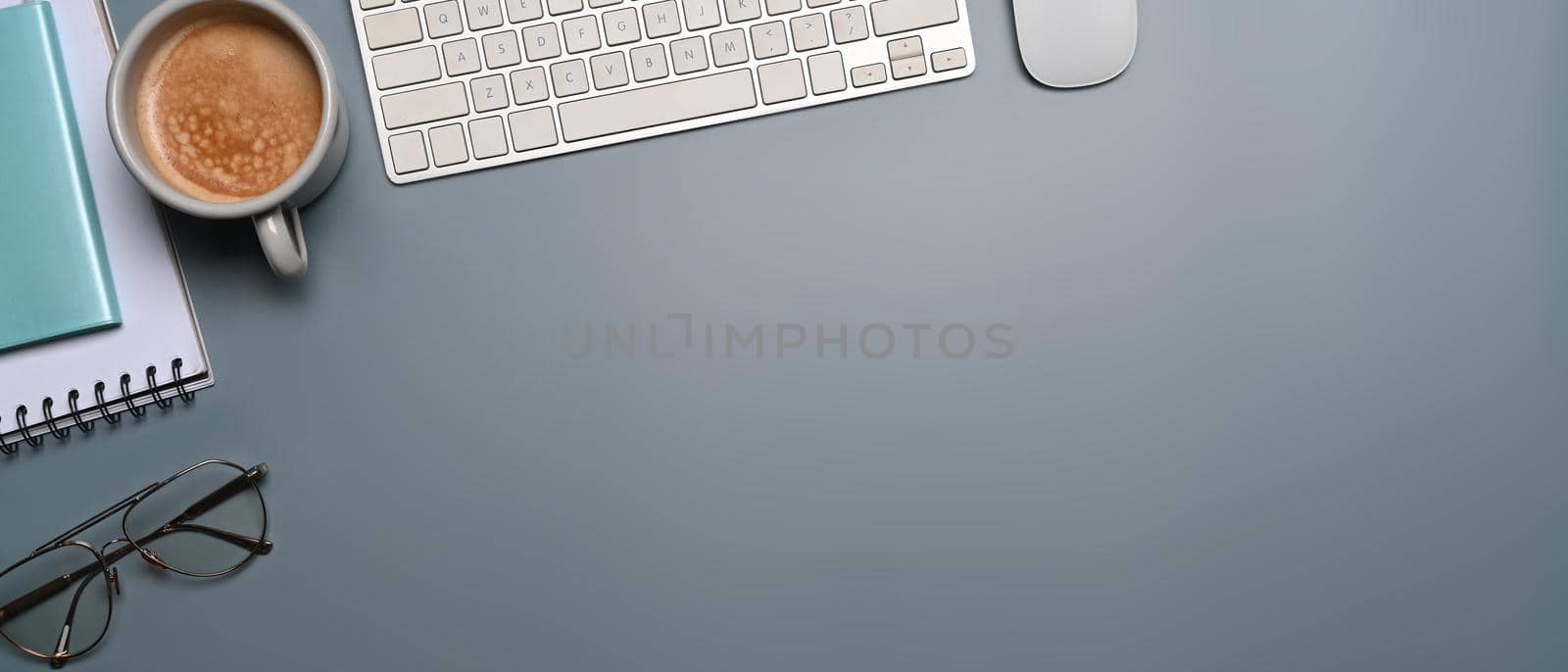 Top view coffee cup, glasses, notebook and wireless keyboard on blue background.