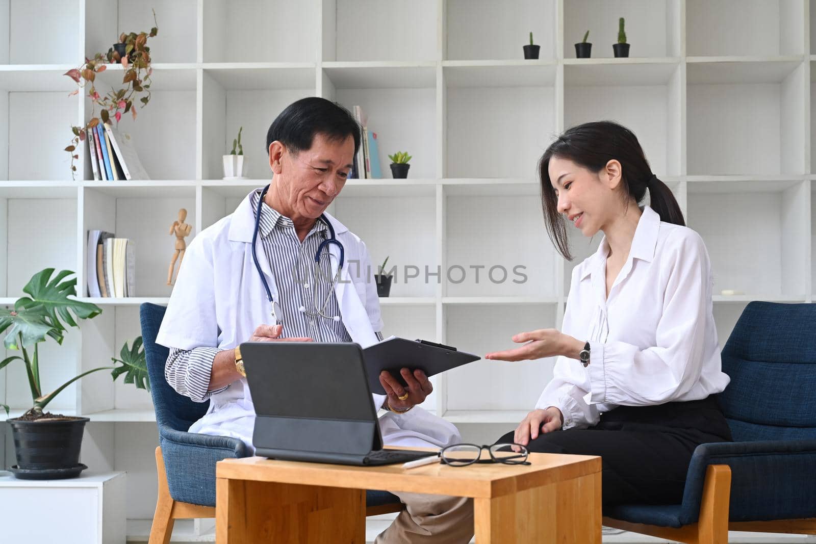 Mature doctor in white uniform consultation with young asian patient in hospital.