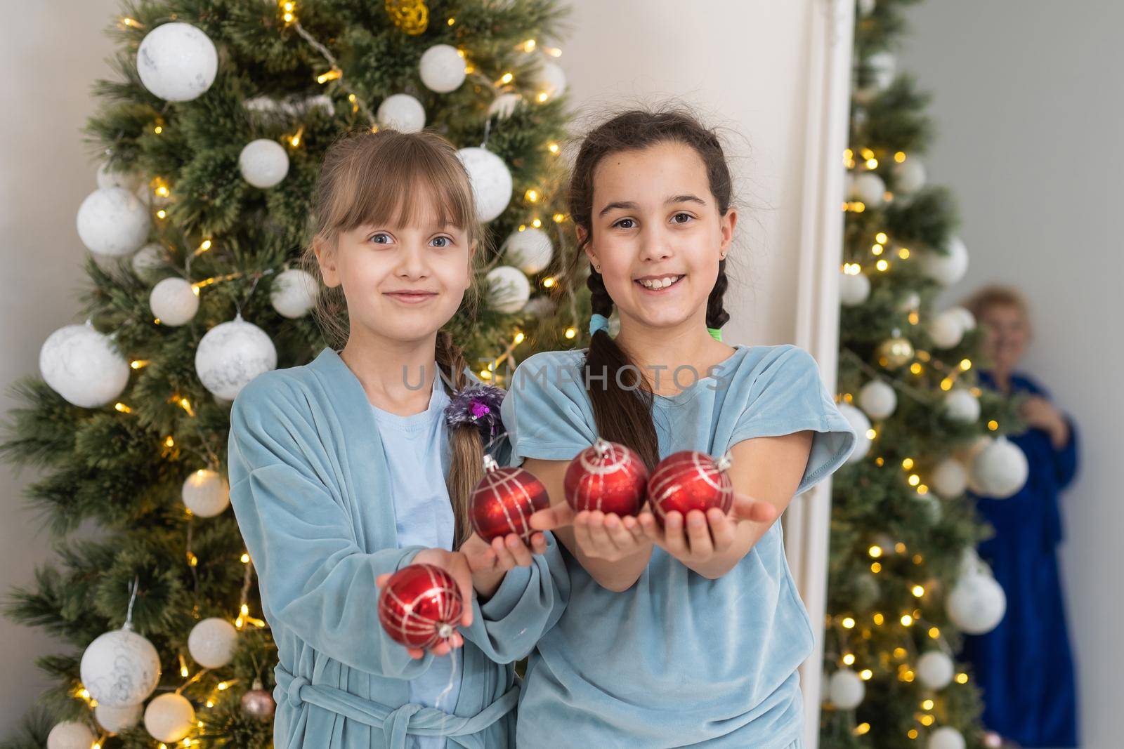 Two little girls open Christmas present under the Christmas tree.