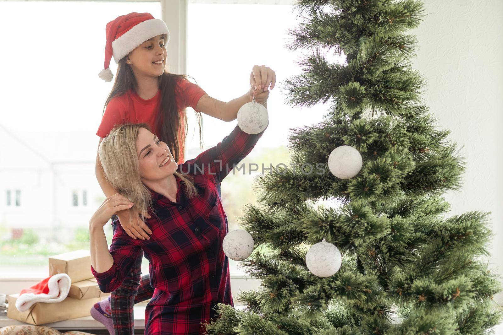 family, winter holidays and people concept - happy mother and little daughter decorating christmas tree at home