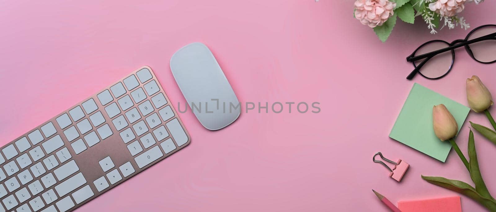Top view wireless keyboard, sticky notes and glasses on pink background.