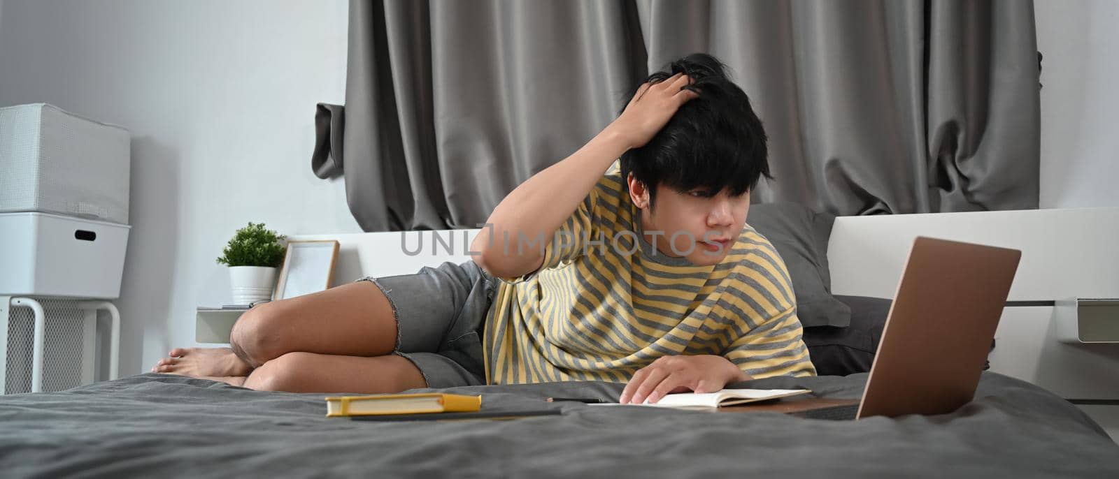 Asian man lying on the bed and study online with laptop computer.